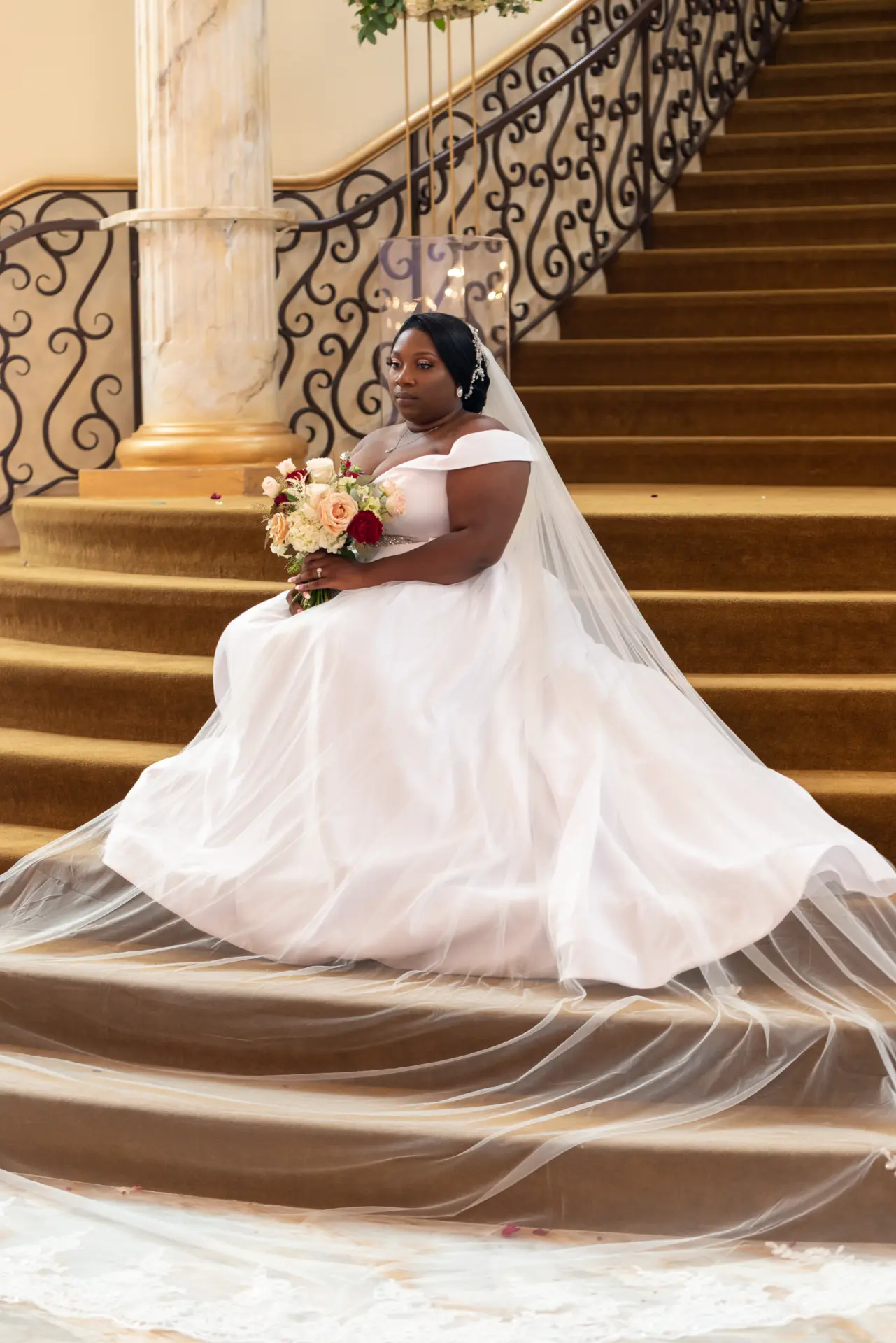 Bride poses on curved stairs with her veil spread across the steps