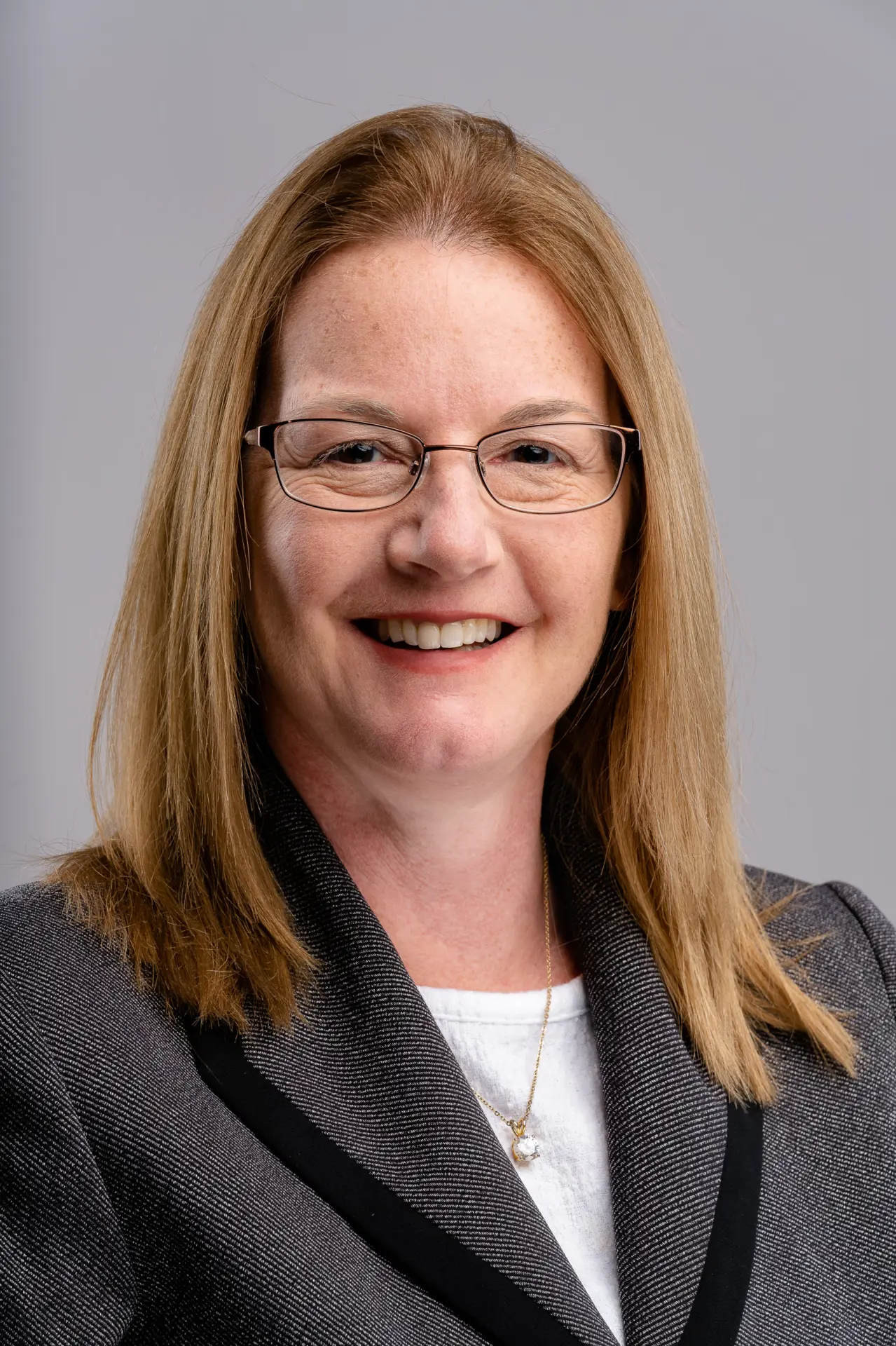 Woman with glasses in a dark blazer, professional headshot on gray