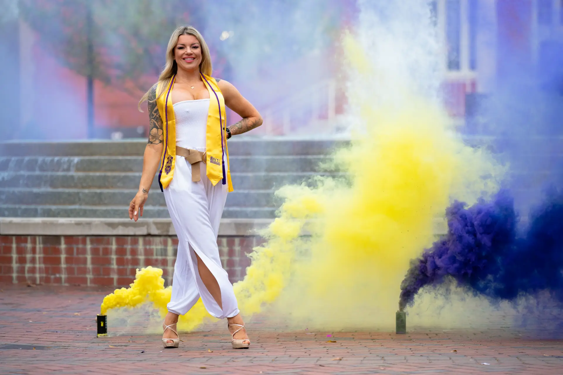 Graduate celebrating amid swirling purple and yellow smoke