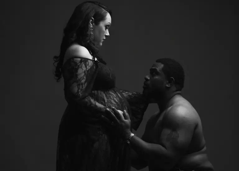 Moody maternity portrait of a couple in shadow, his hand on her bump