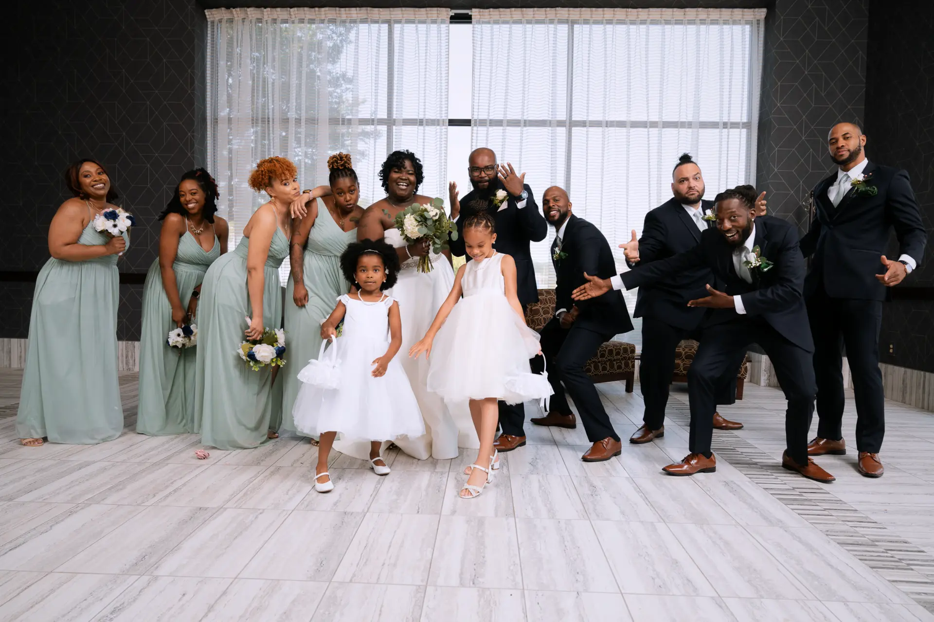 Wedding party poses in a bright reception room with tall windows