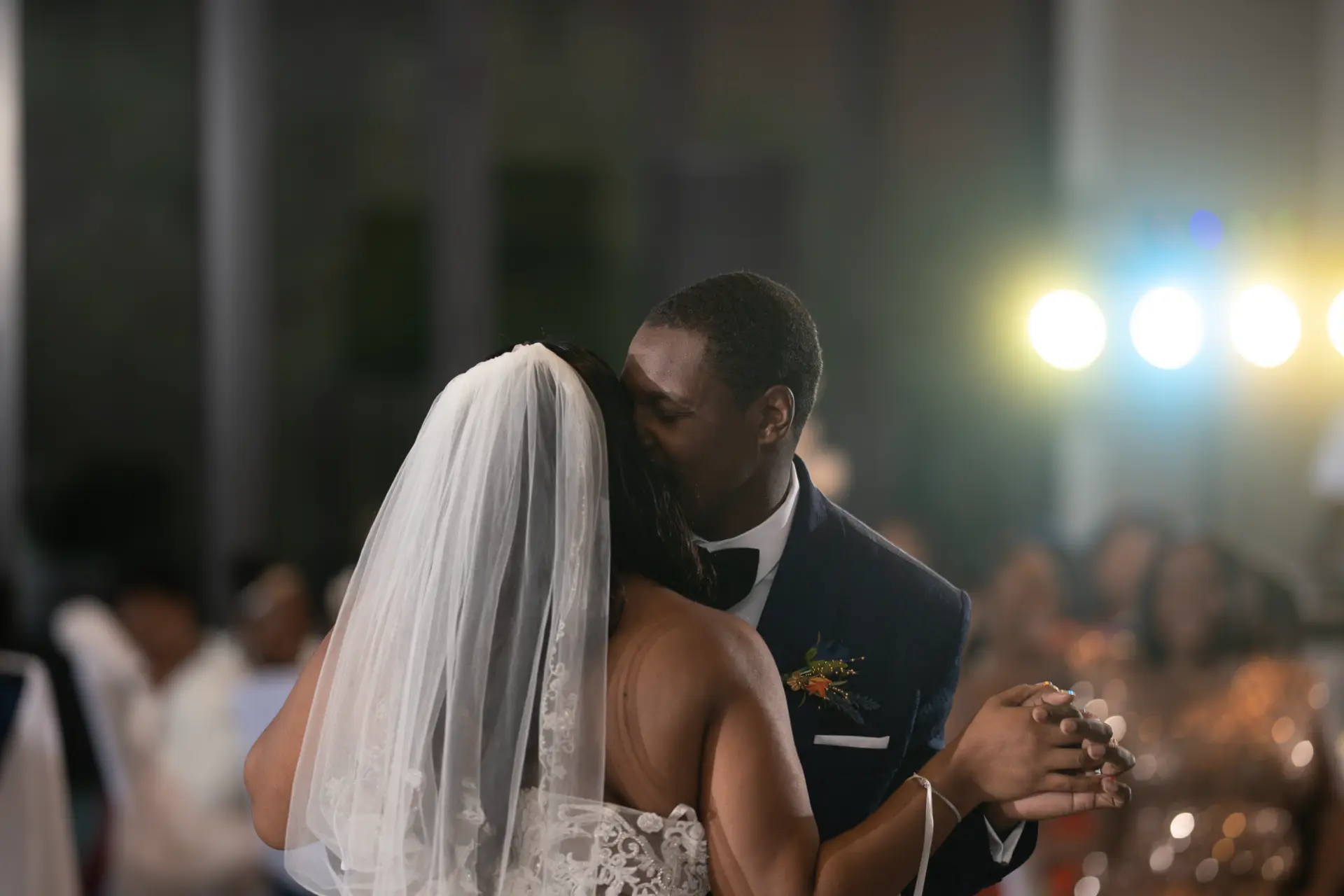 Bride in a long veil faces the groom under stage lights