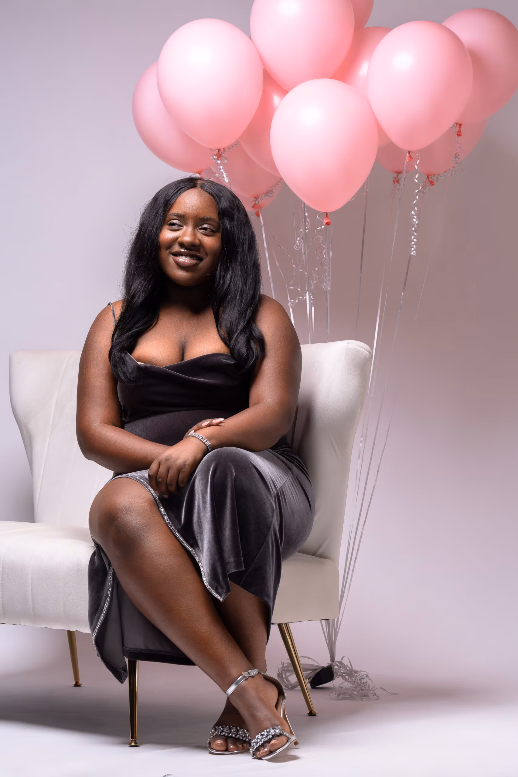 Woman seated in a white chair holding pink balloons
