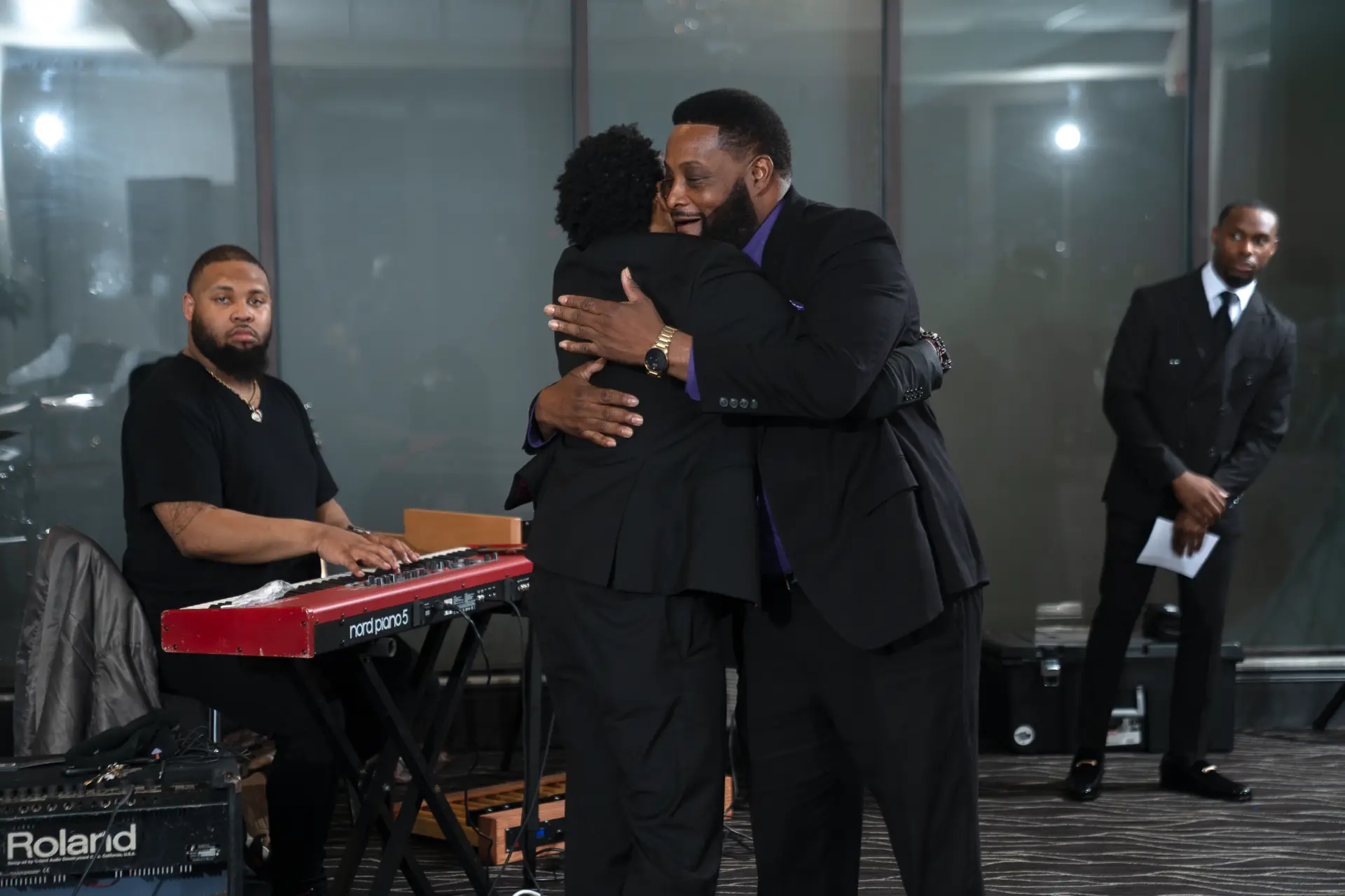 Performers in black on stage with a keyboardist at a formal event