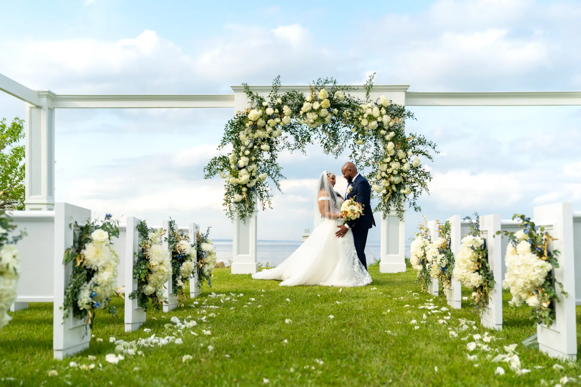 Outdoor ceremony under a white floral arch on a green lawn