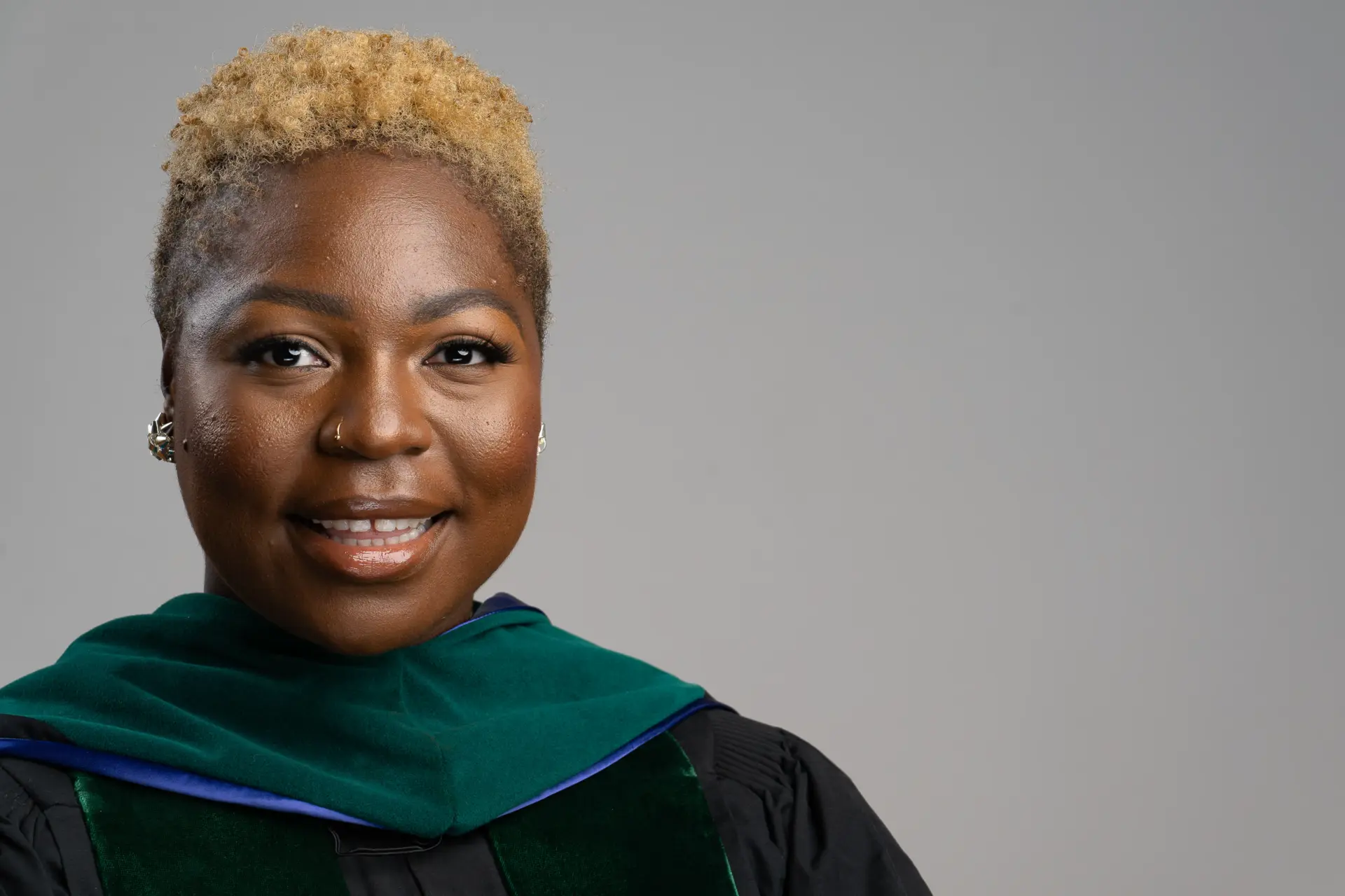 Woman with short blond hair in green doctoral regalia, studio headshot