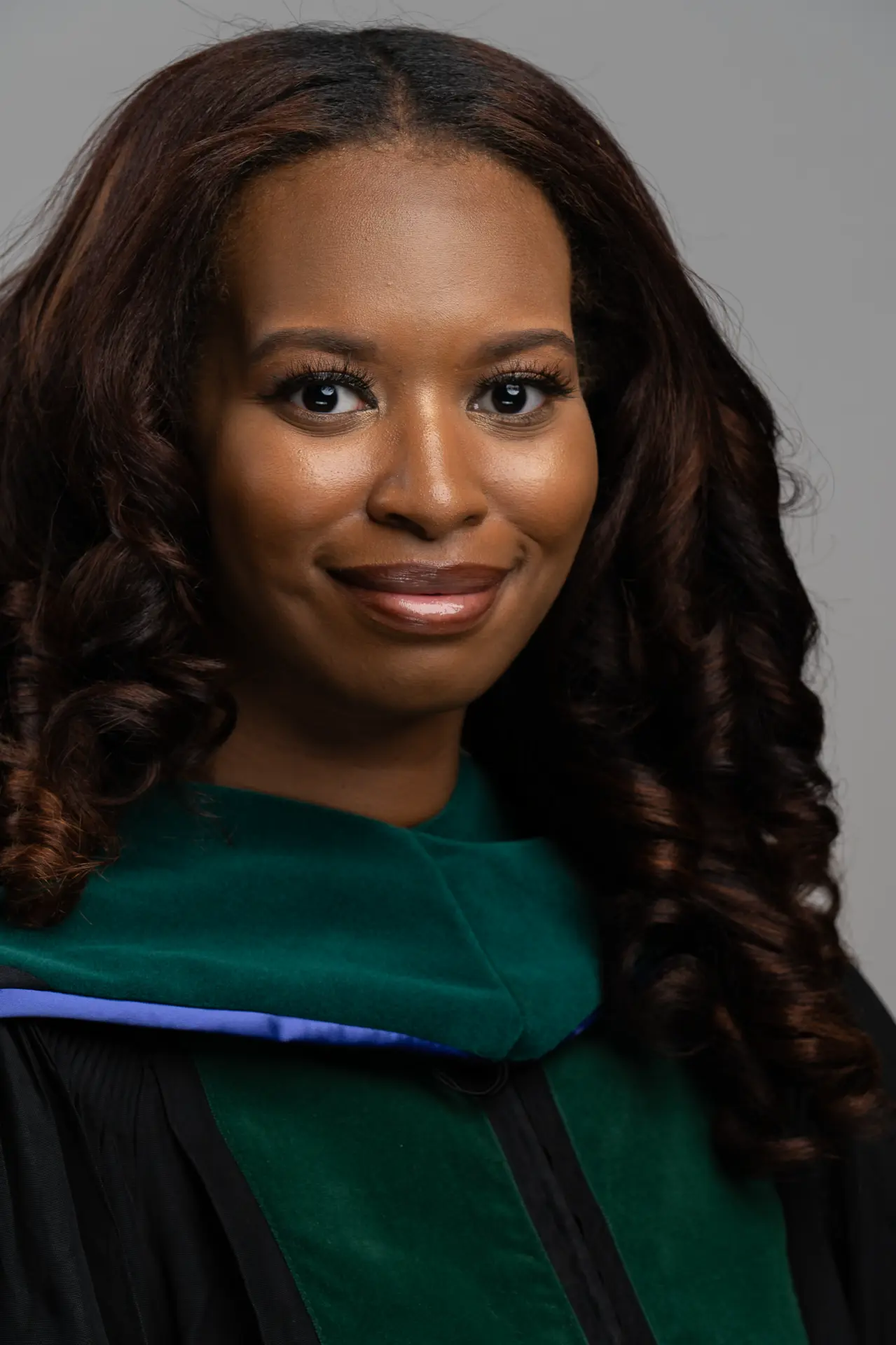 Smiling woman in green doctoral regalia, studio headshot