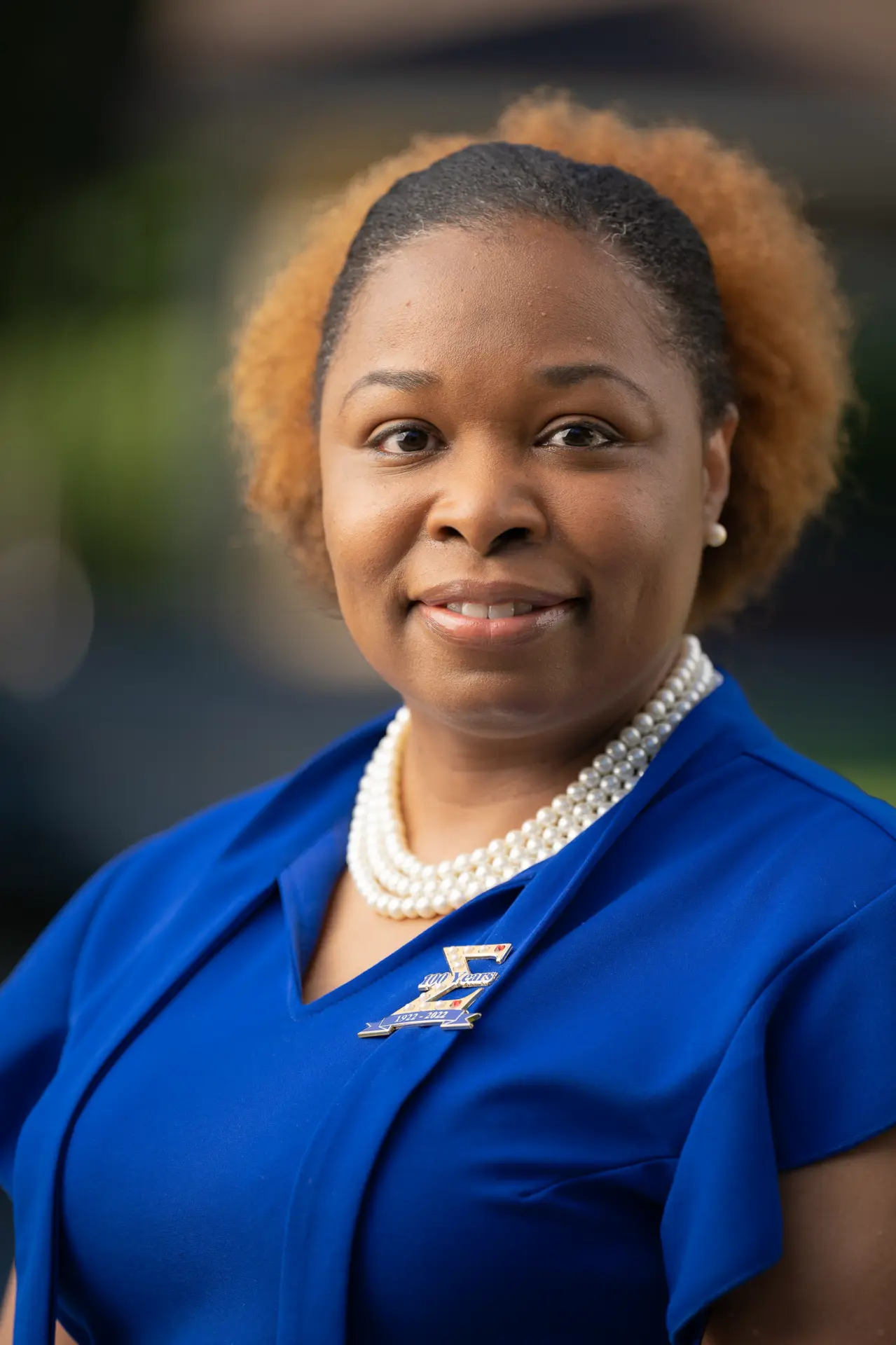 Smiling woman in a royal blue top, outdoor headshot