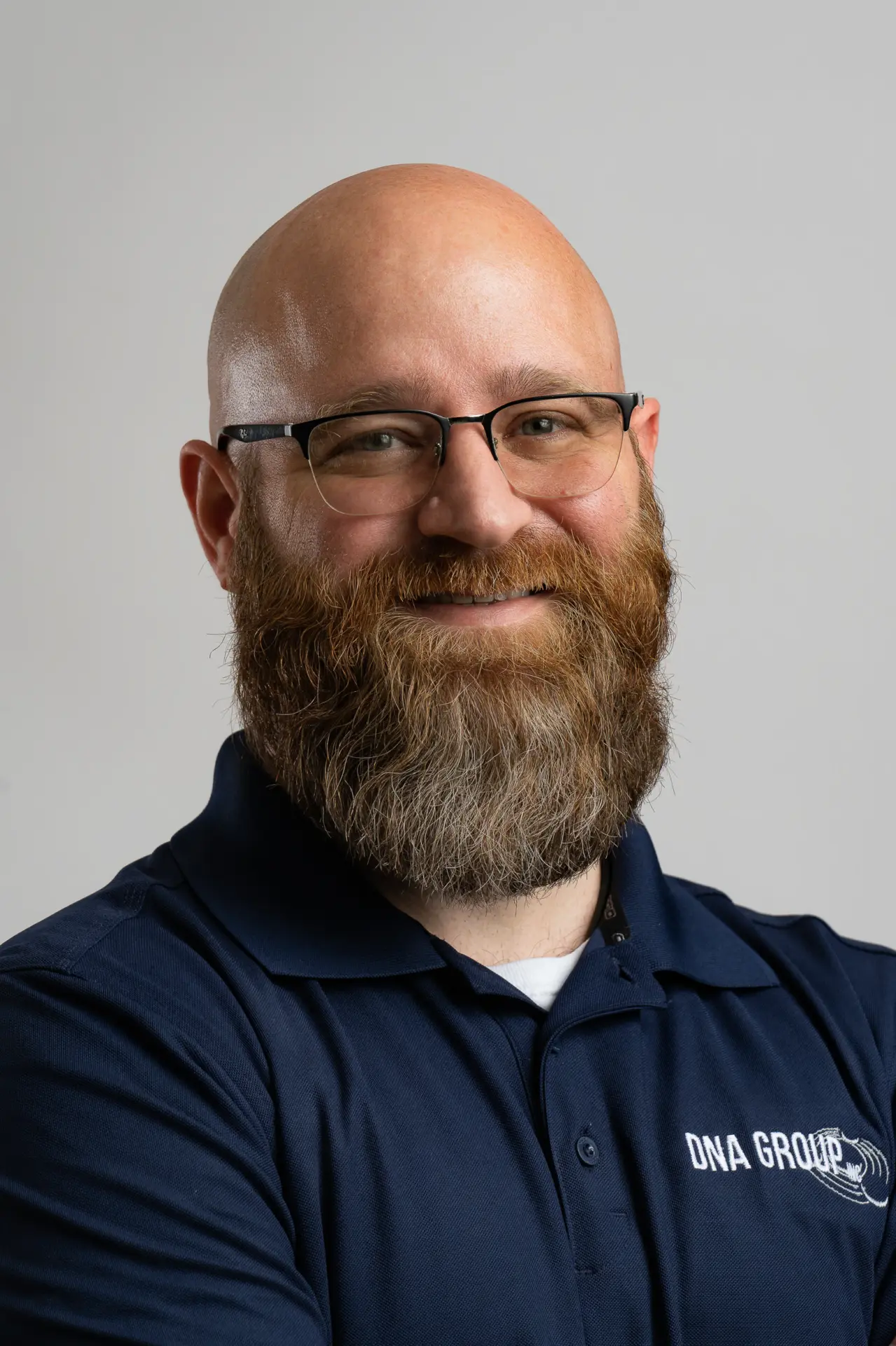 Bearded man with glasses in a navy polo, business headshot