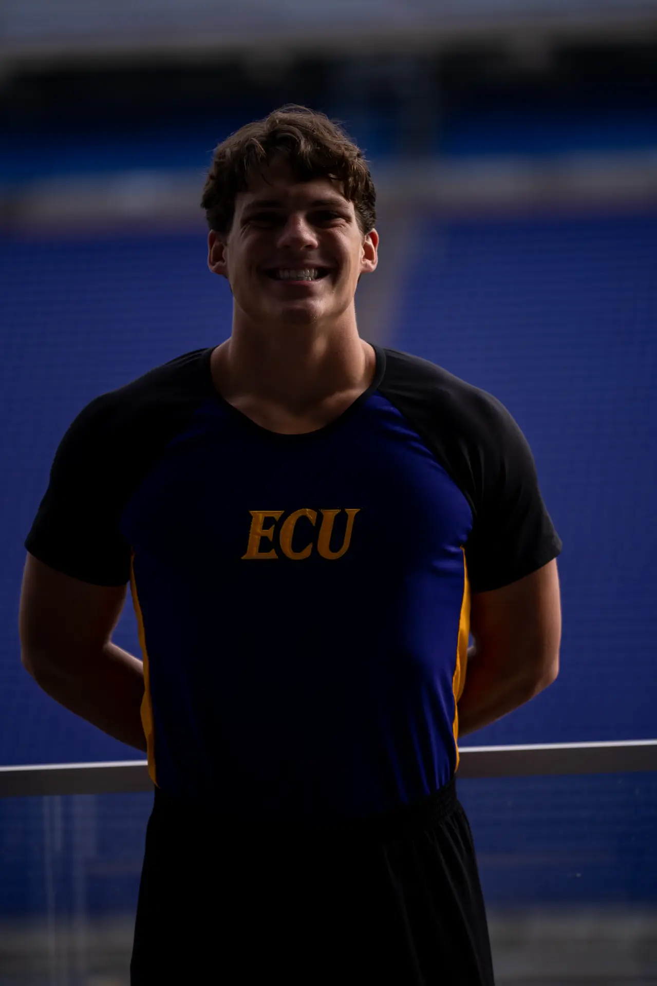 ECU cheerleader in a navy and purple uniform, stadium team portrait