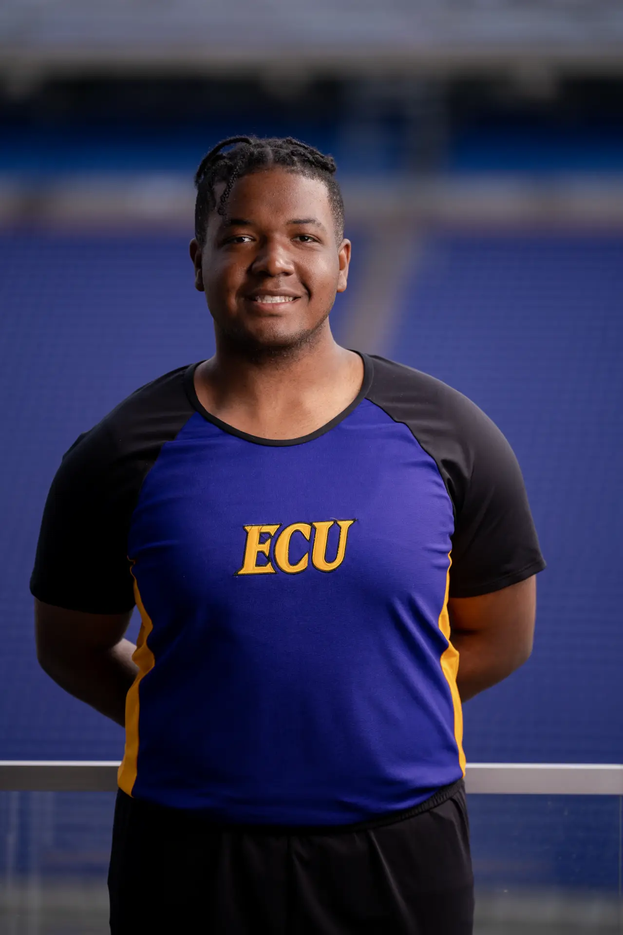 Male ECU cheerleader in a purple uniform smiling in the stadium