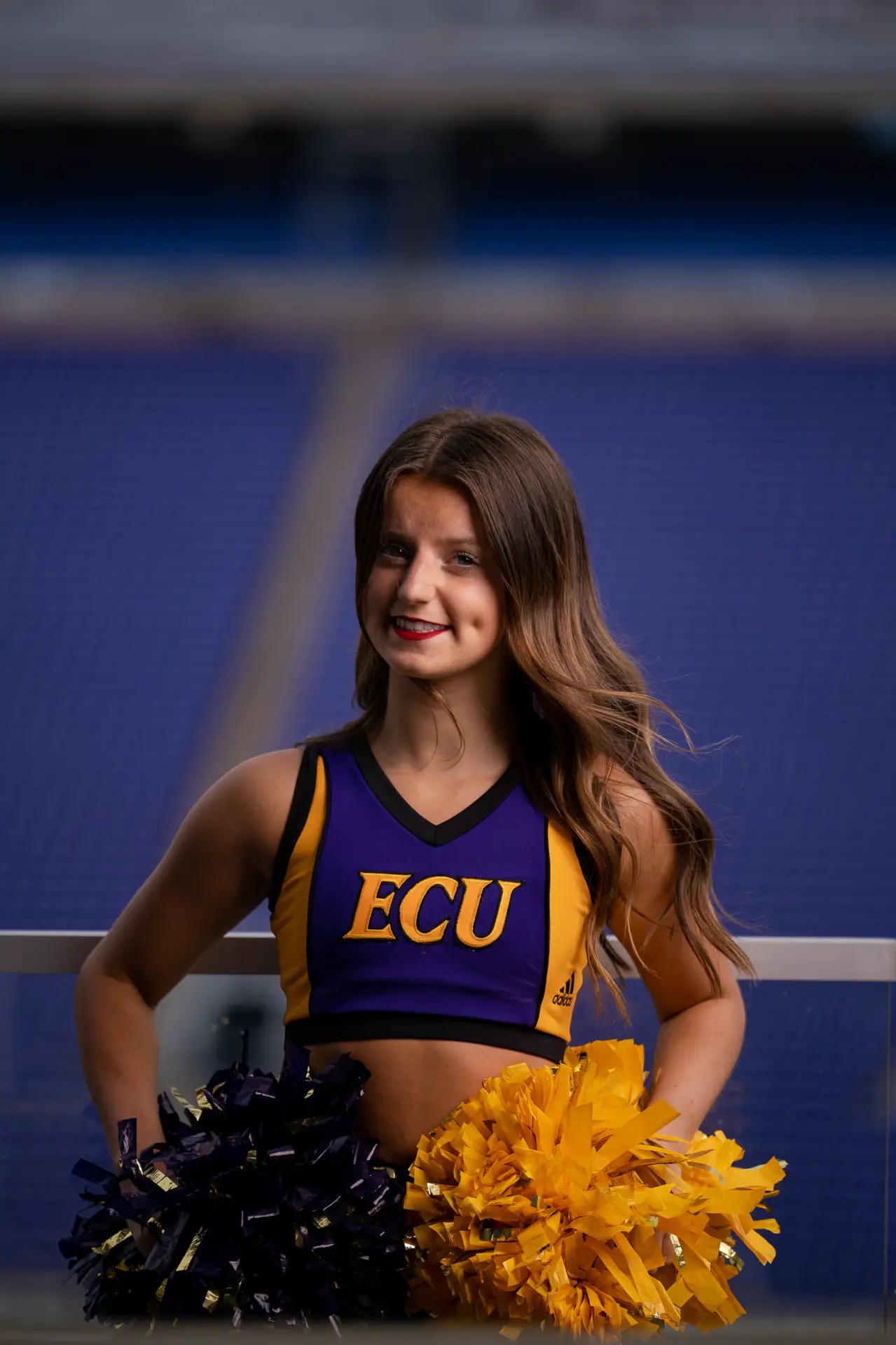 Cheerleader in an ECU uniform smiling on the football field