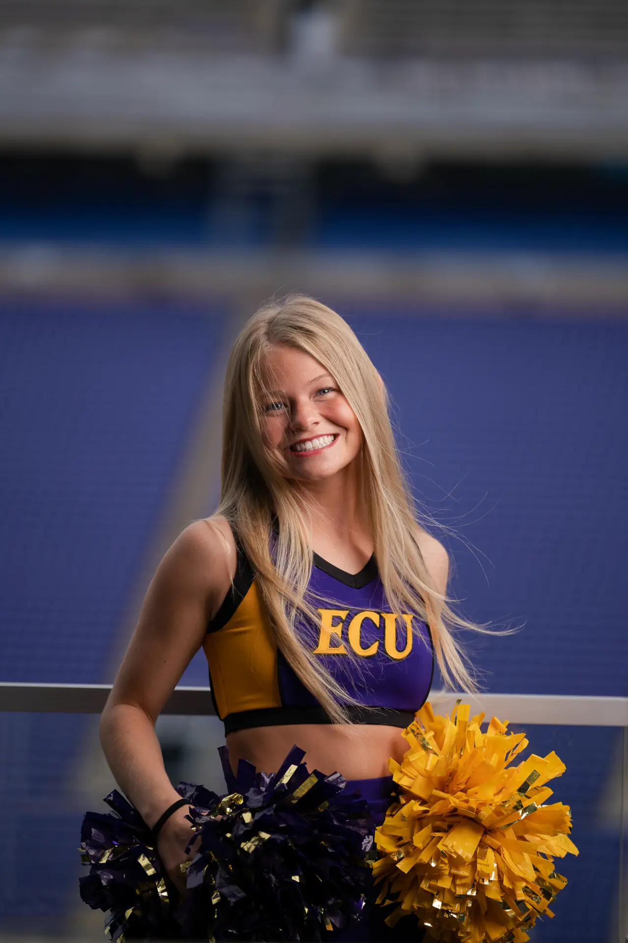 Cheerleader in an ECU uniform smiling on the football field