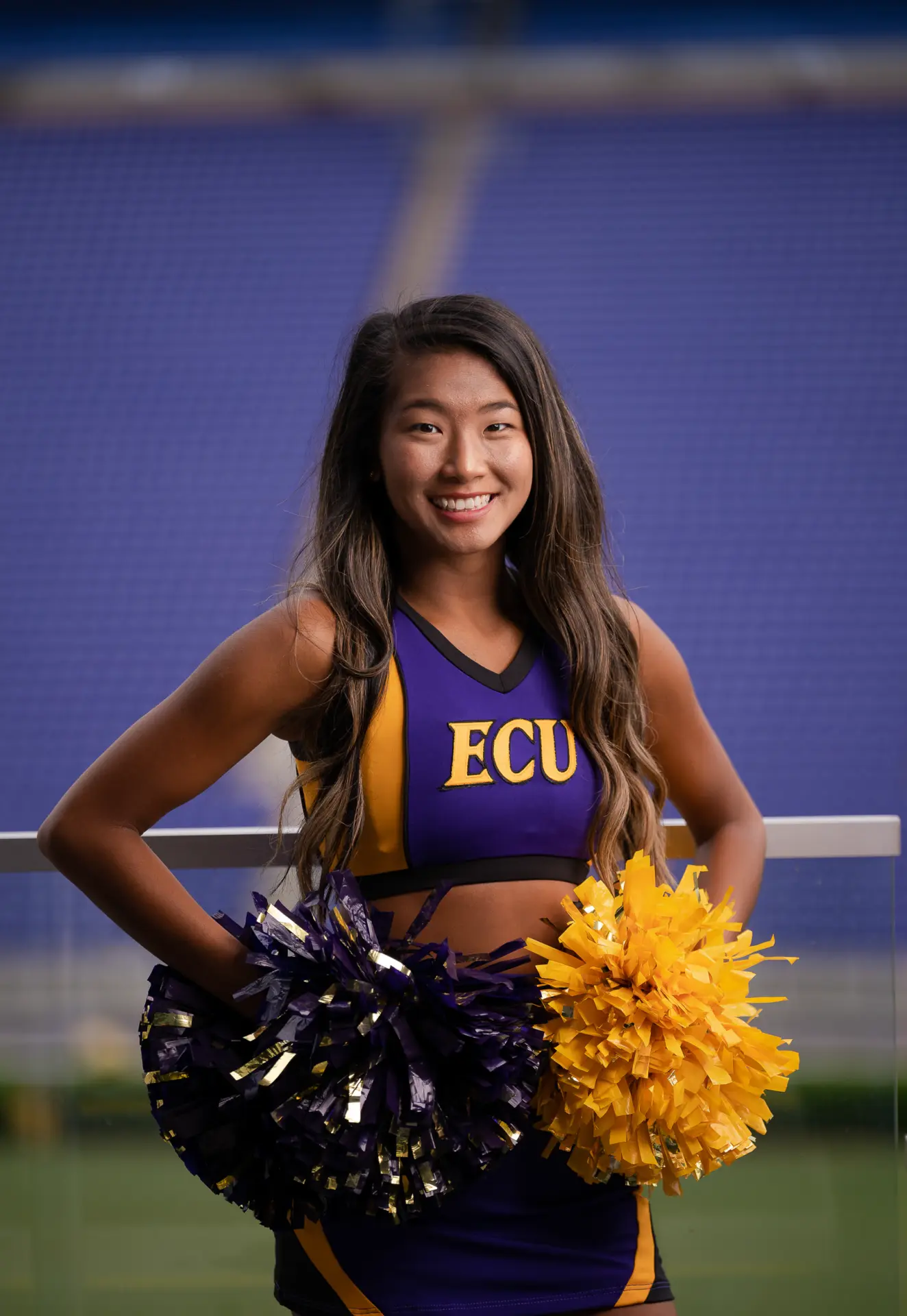 ECU cheerleader in uniform smiling on the stadium turf