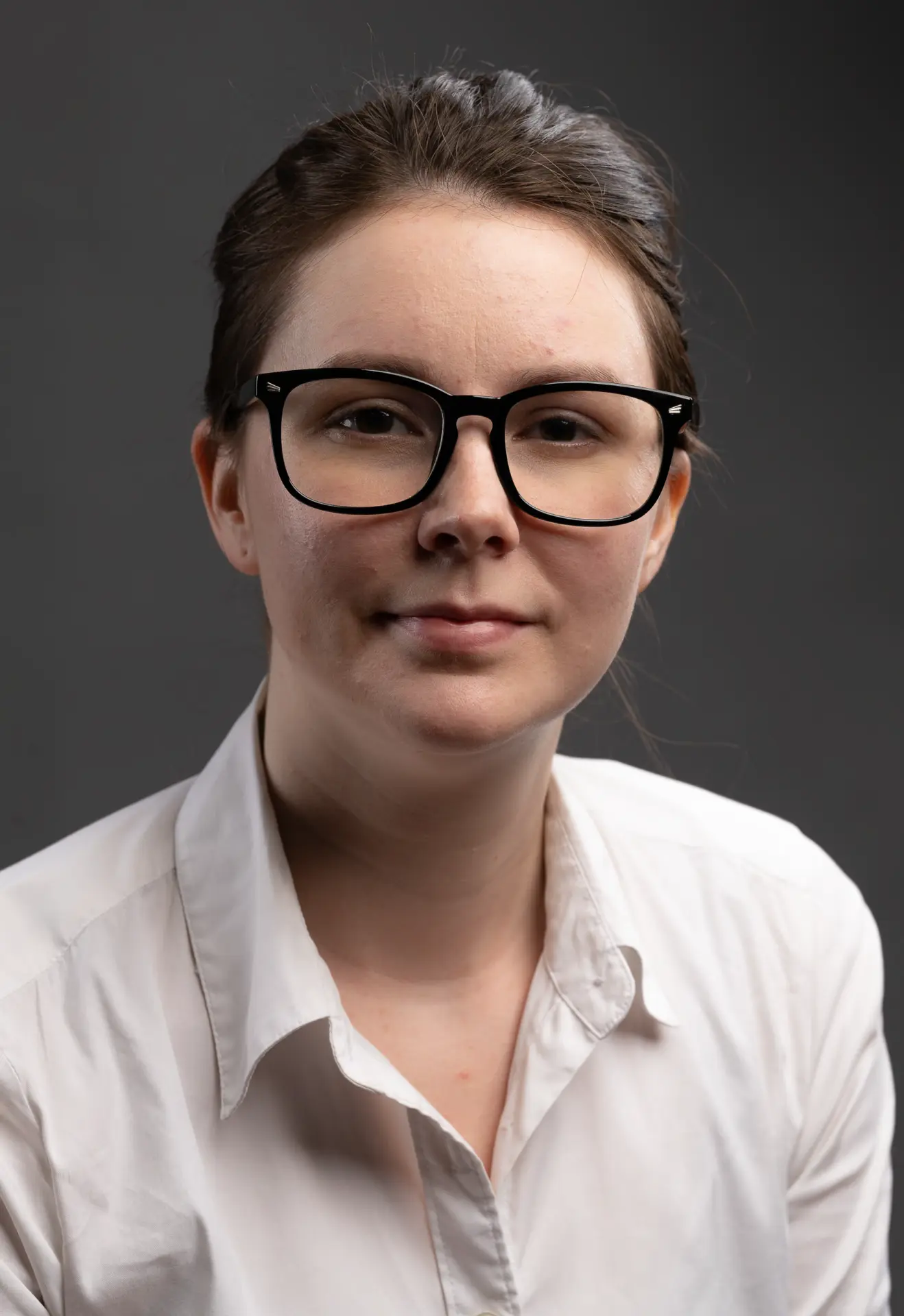 Woman with glasses in a white collared shirt, studio headshot