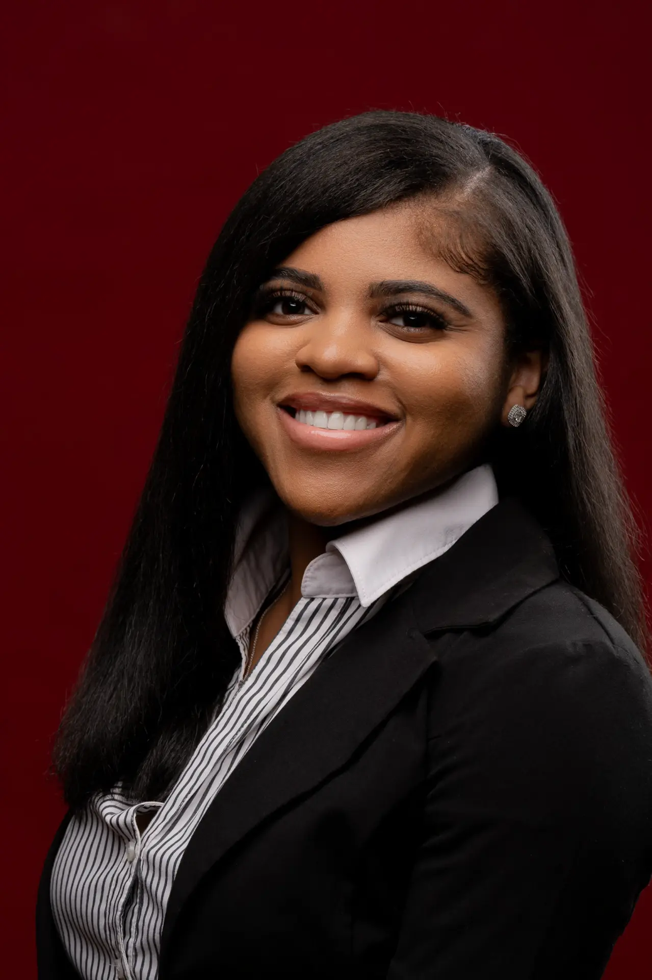 Smiling woman in a black blazer against a deep red backdrop
