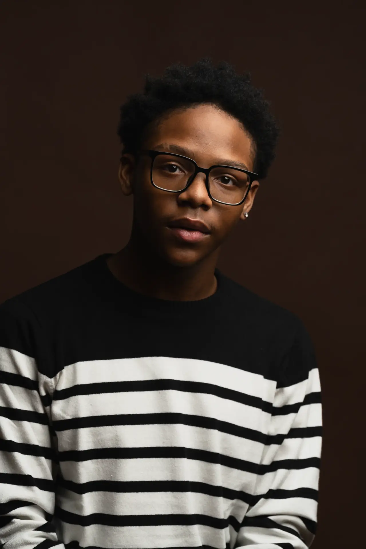 Young man in glasses and a striped sweater against a dark backdrop