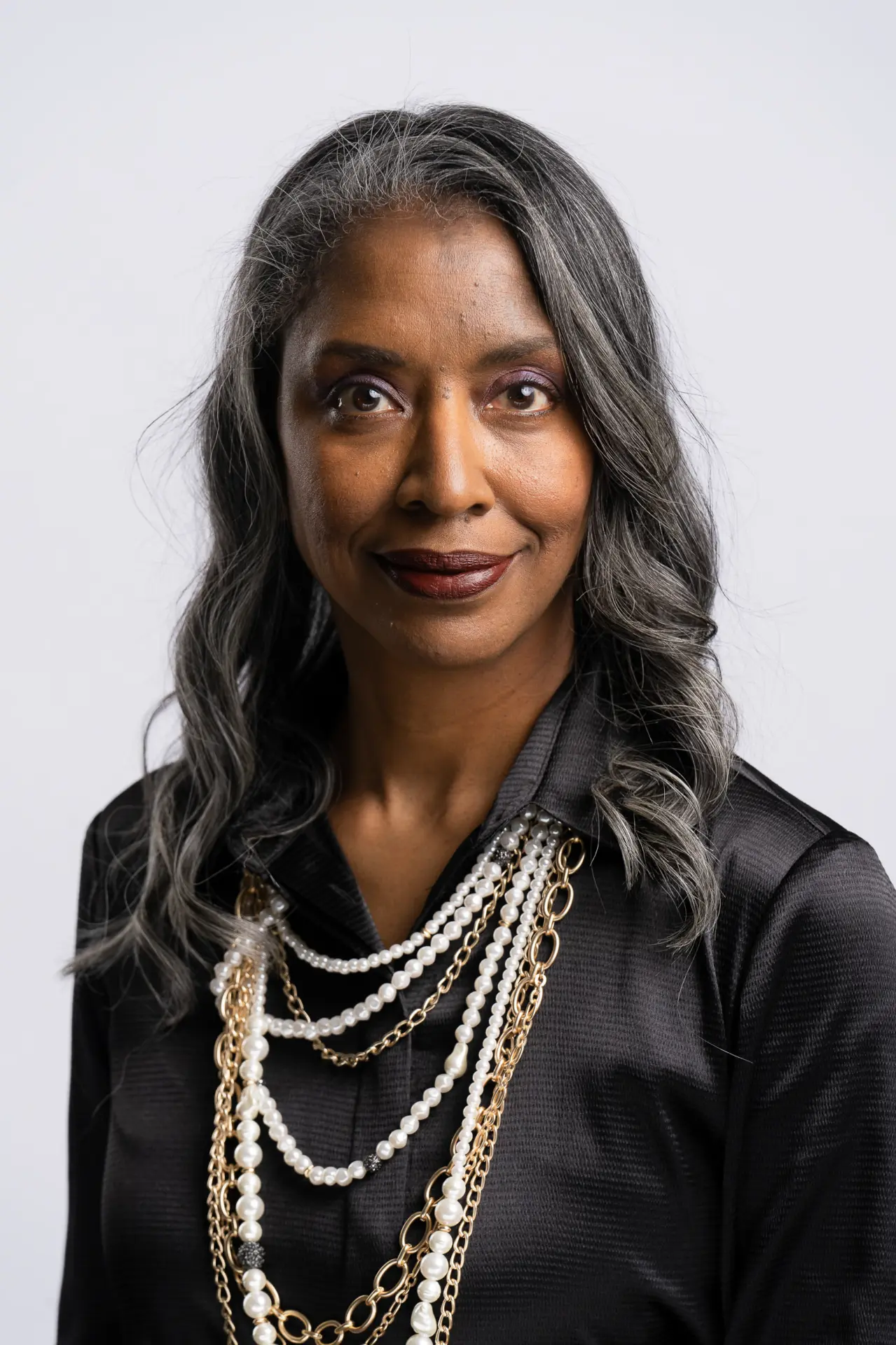Woman with long silver hair and pearls in black, studio portrait