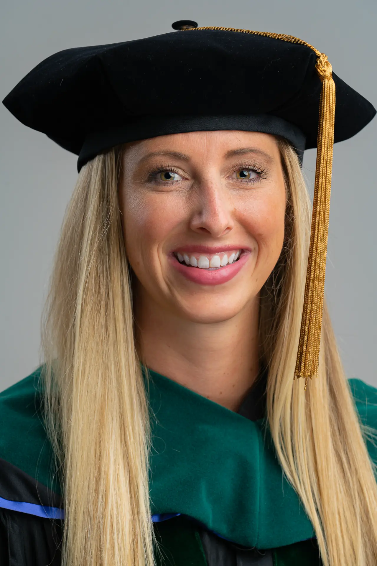 Smiling woman in a doctoral tam and green regalia, studio headshot