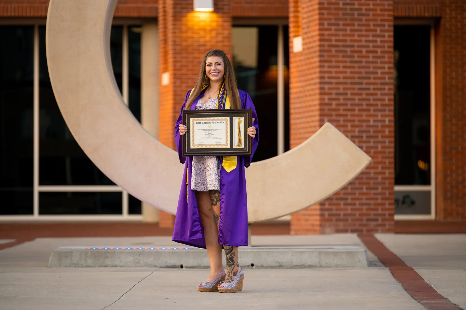 Graduate holding her diploma in front of the ECU C sculpture