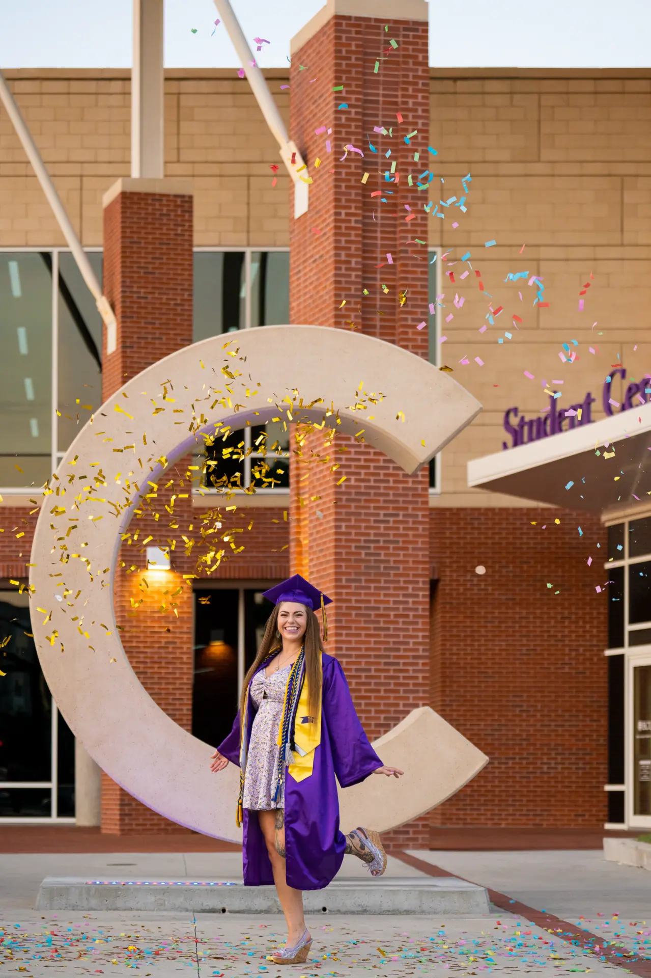 Graduate in a purple gown standing inside the ECU letter C sculpture