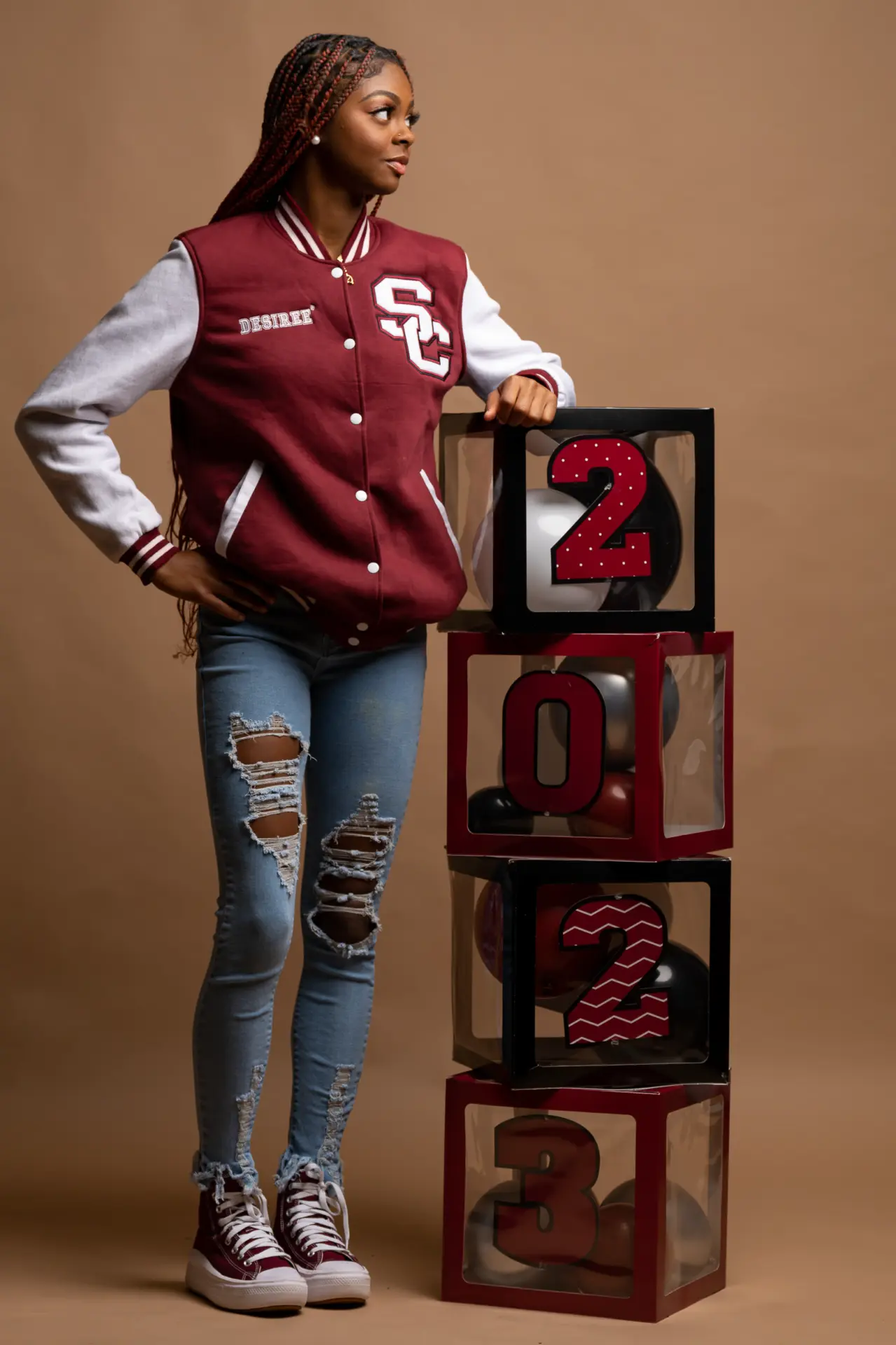 Graduate in a varsity jacket beside stacked letter blocks