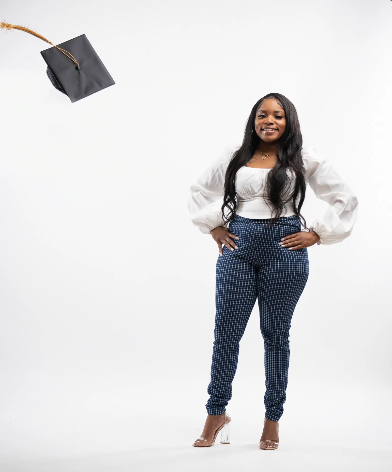 Graduate in jeans tossing her cap in a white studio