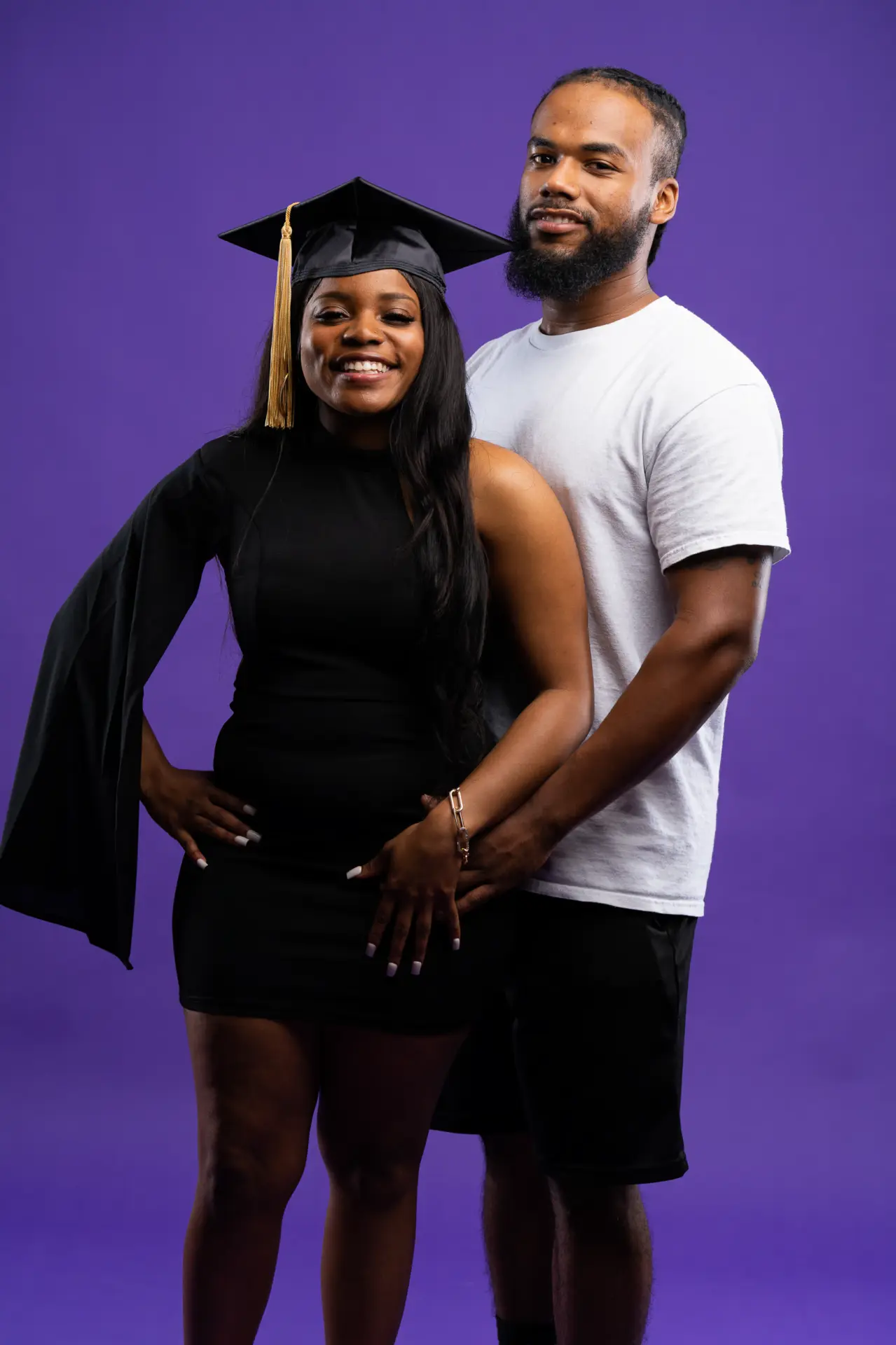 Graduating couple in cap and gown on a purple studio backdrop