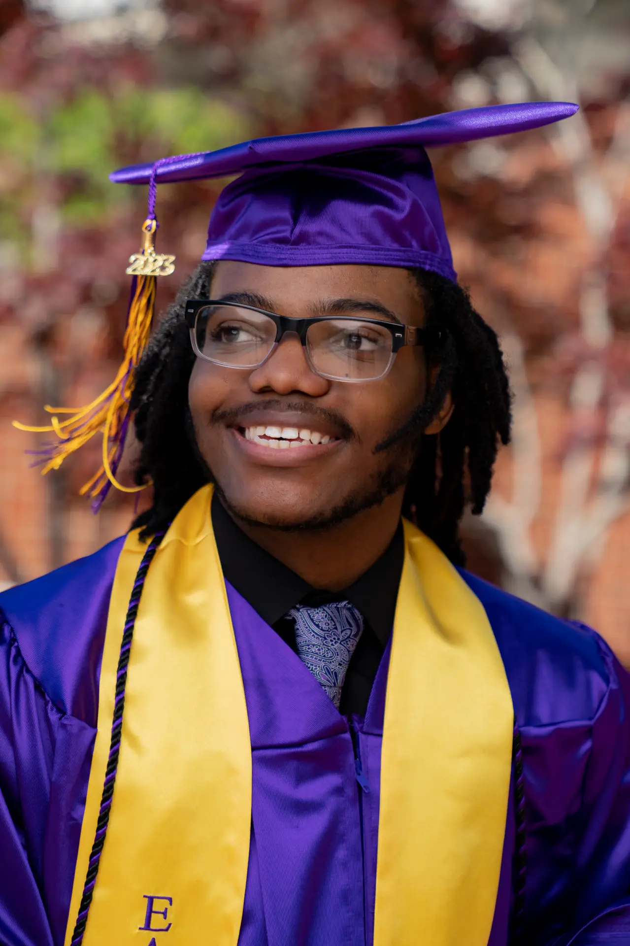 Smiling graduate in a purple cap and gold stole, close portrait