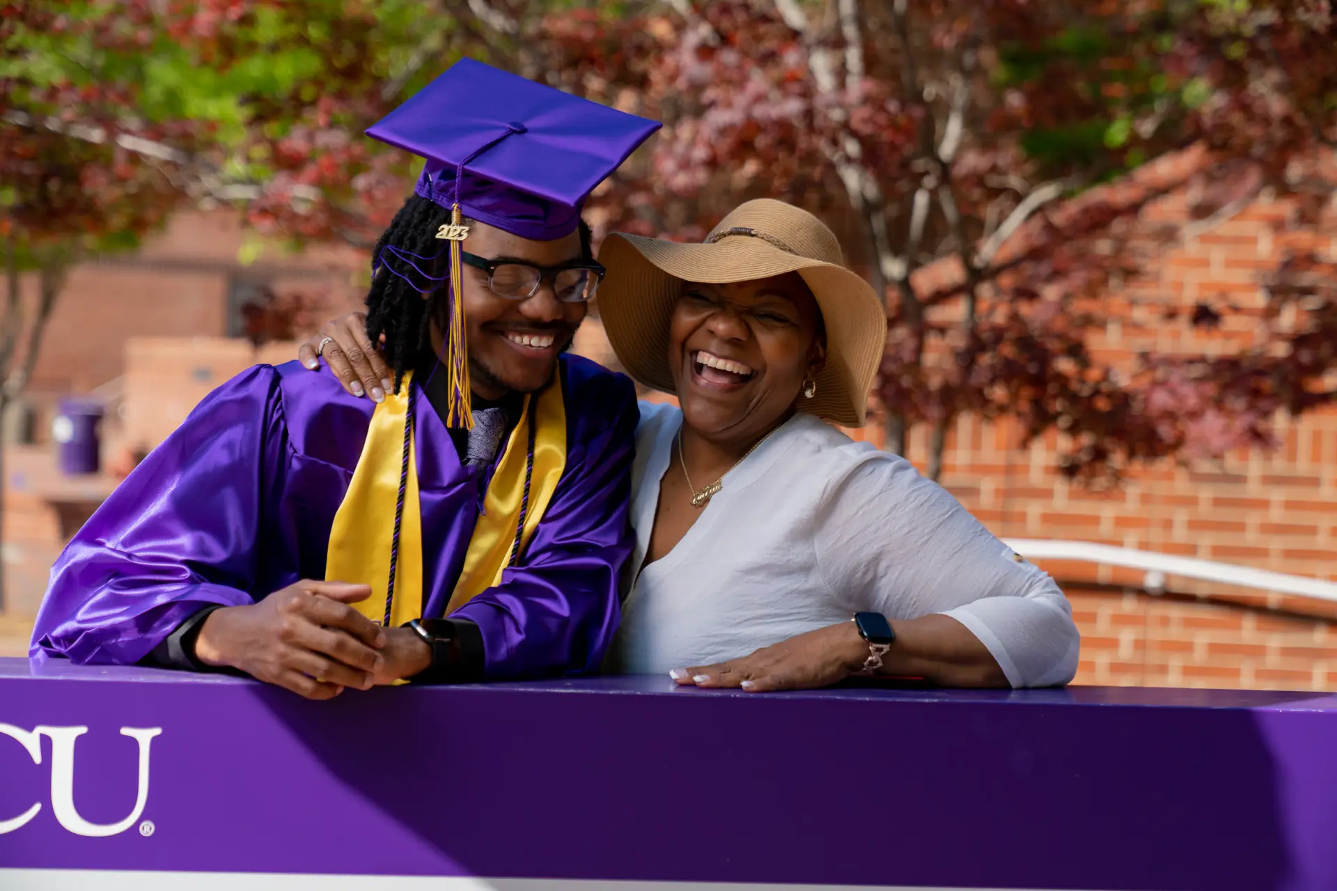 Graduate in a purple gown with a friend beside an ECU banner