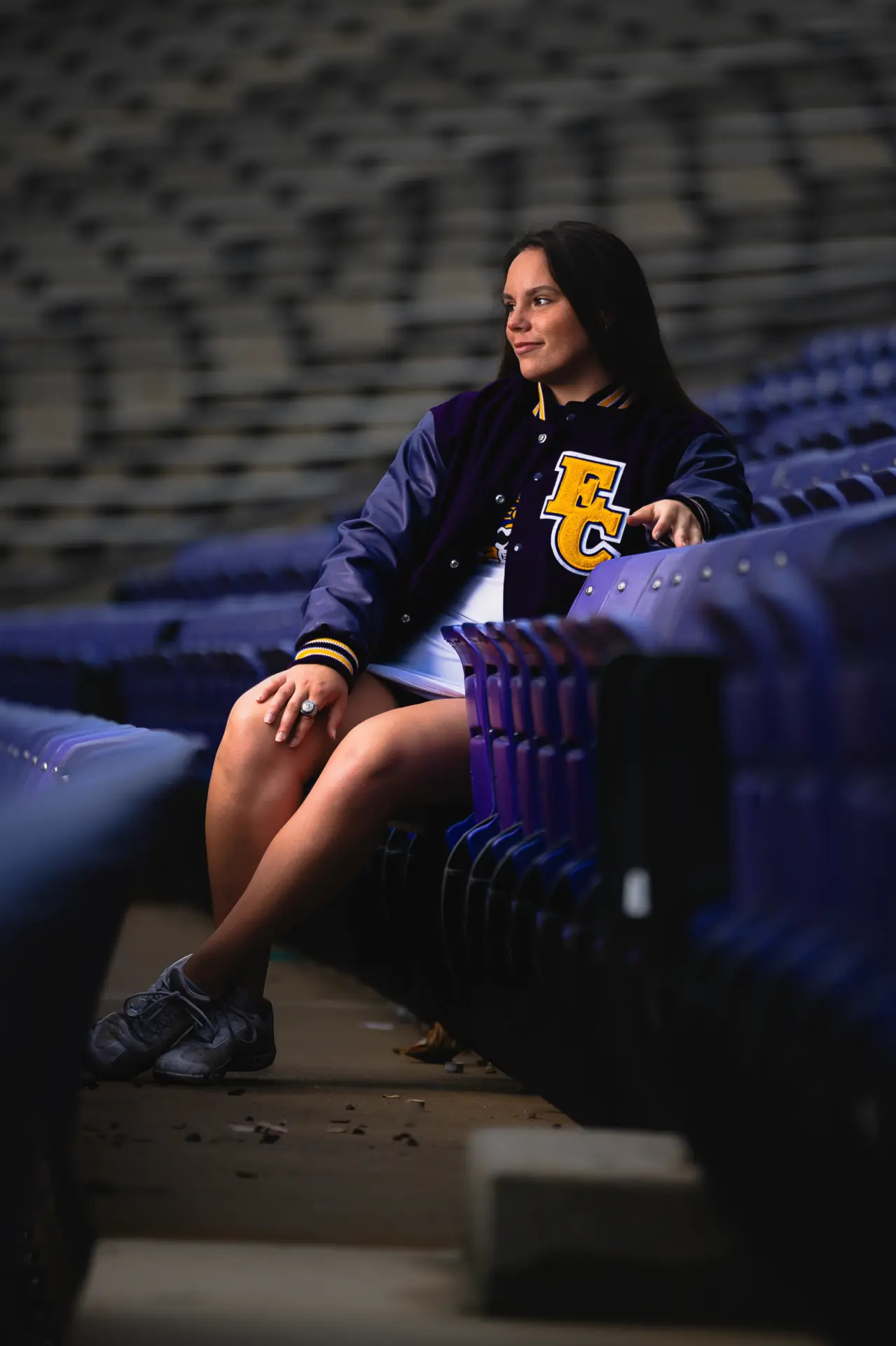 Graduate in an ECU sweatshirt seated in empty stadium bleachers
