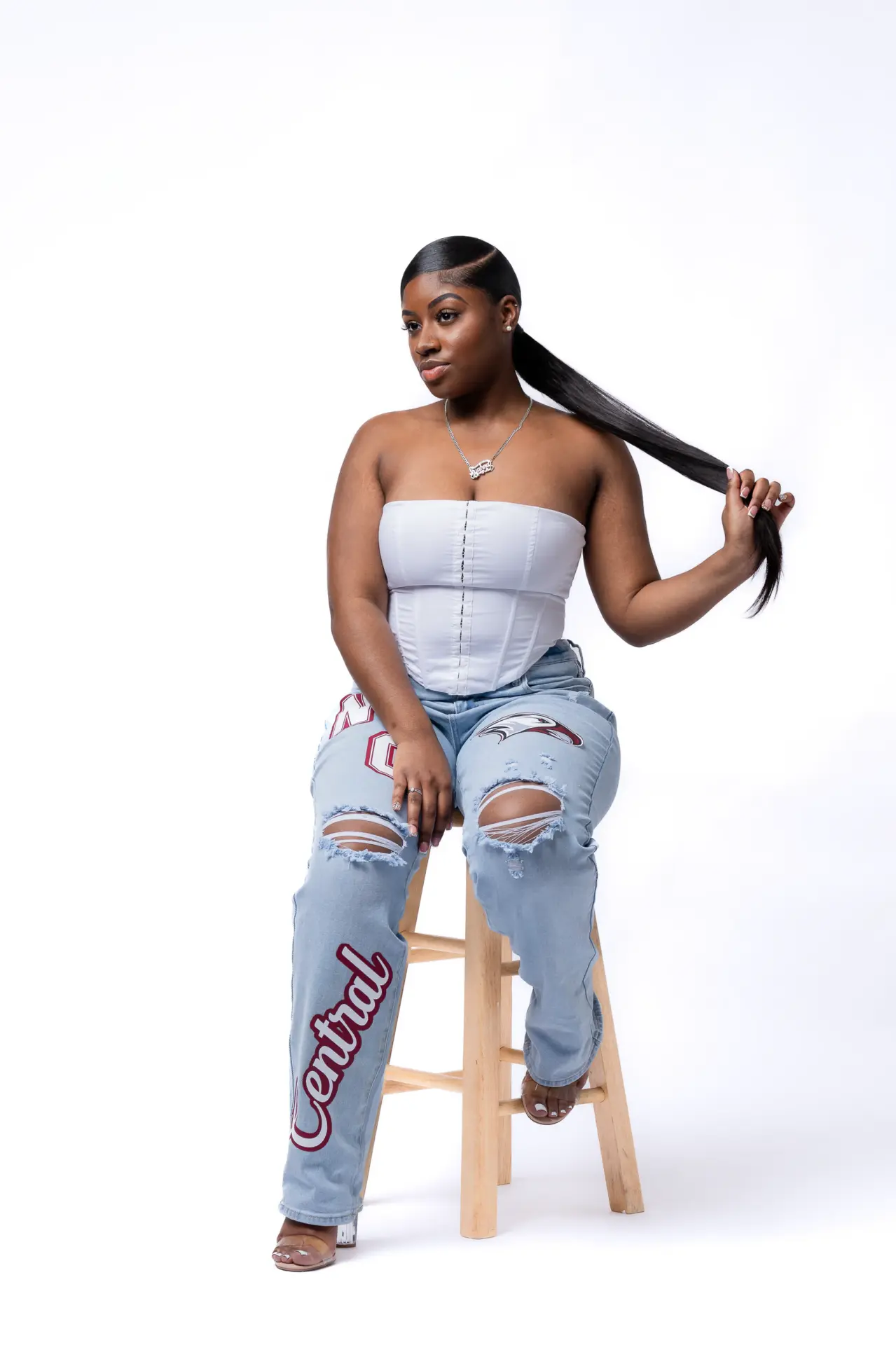 Graduate in jeans seated on a stool, bright studio portrait