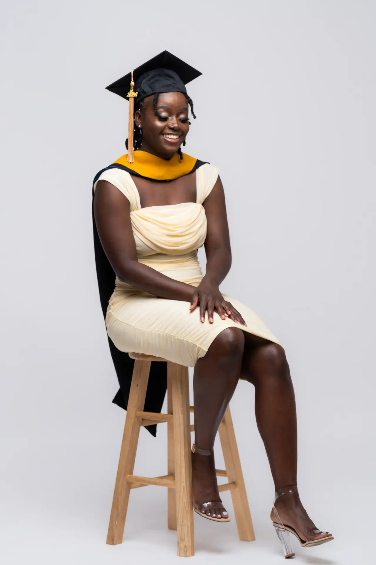 Graduate in a gold dress seated on a stool in a white studio