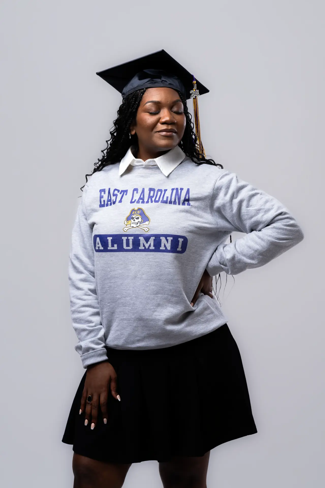 Graduate in a cap and alma mater sweatshirt in a gray studio