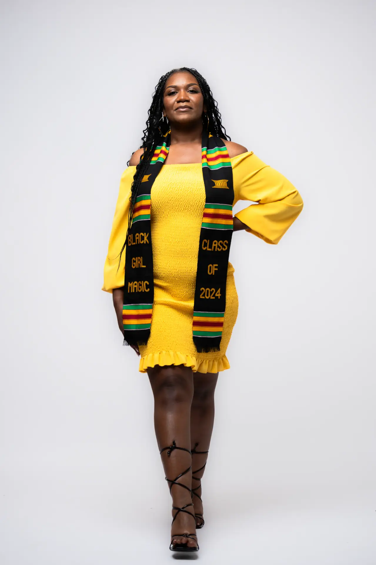 Graduate in a yellow dress and kente stole, white studio portrait
