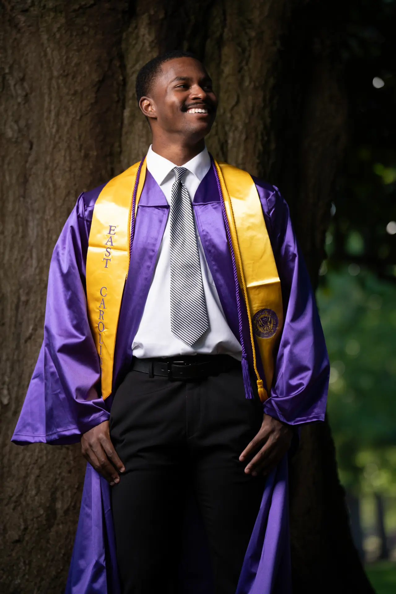 Male graduate in a purple gown and gold stole, close portrait outdoors