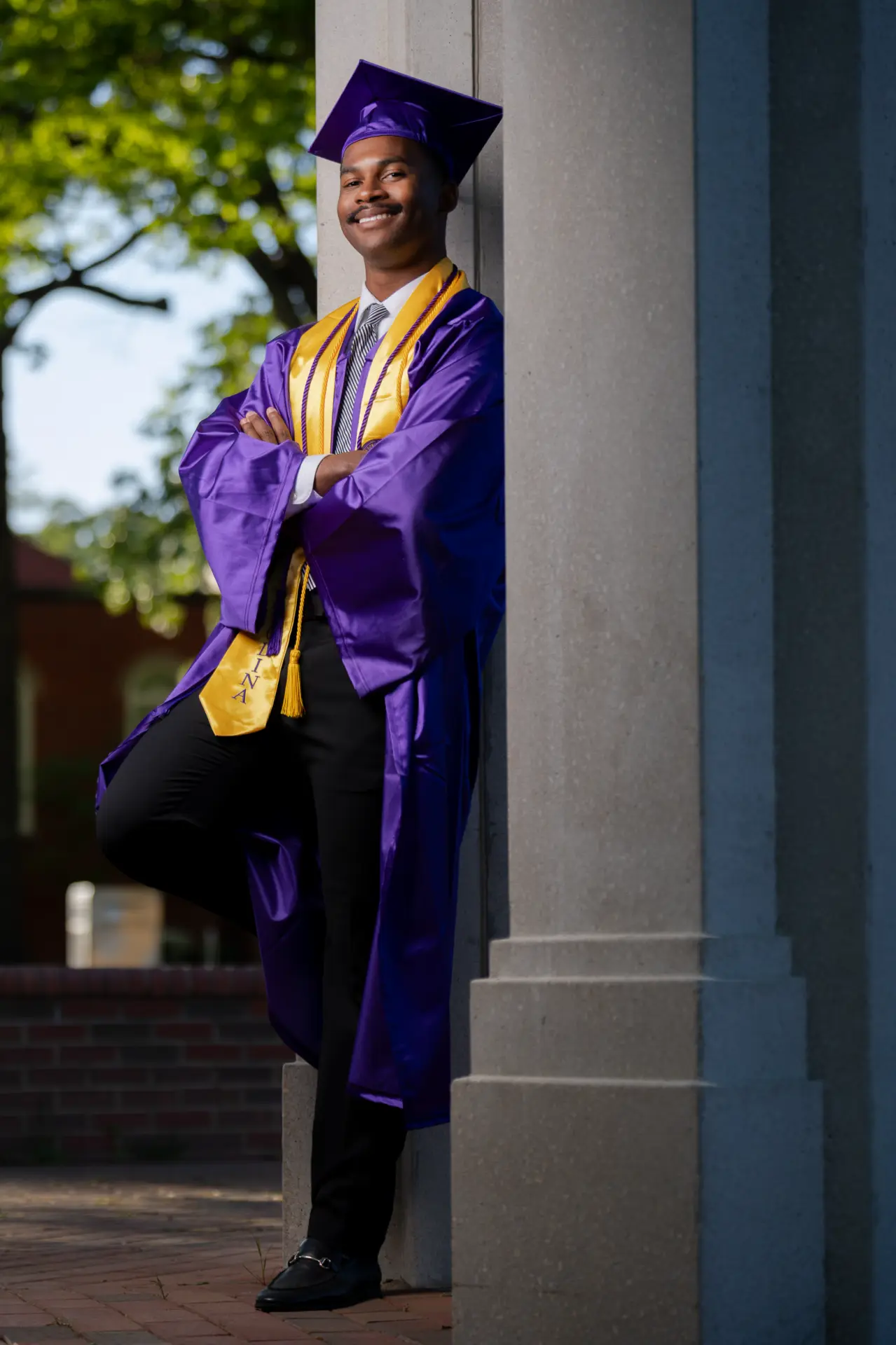 Graduate in cap and purple gown framed by campus columns at sunset