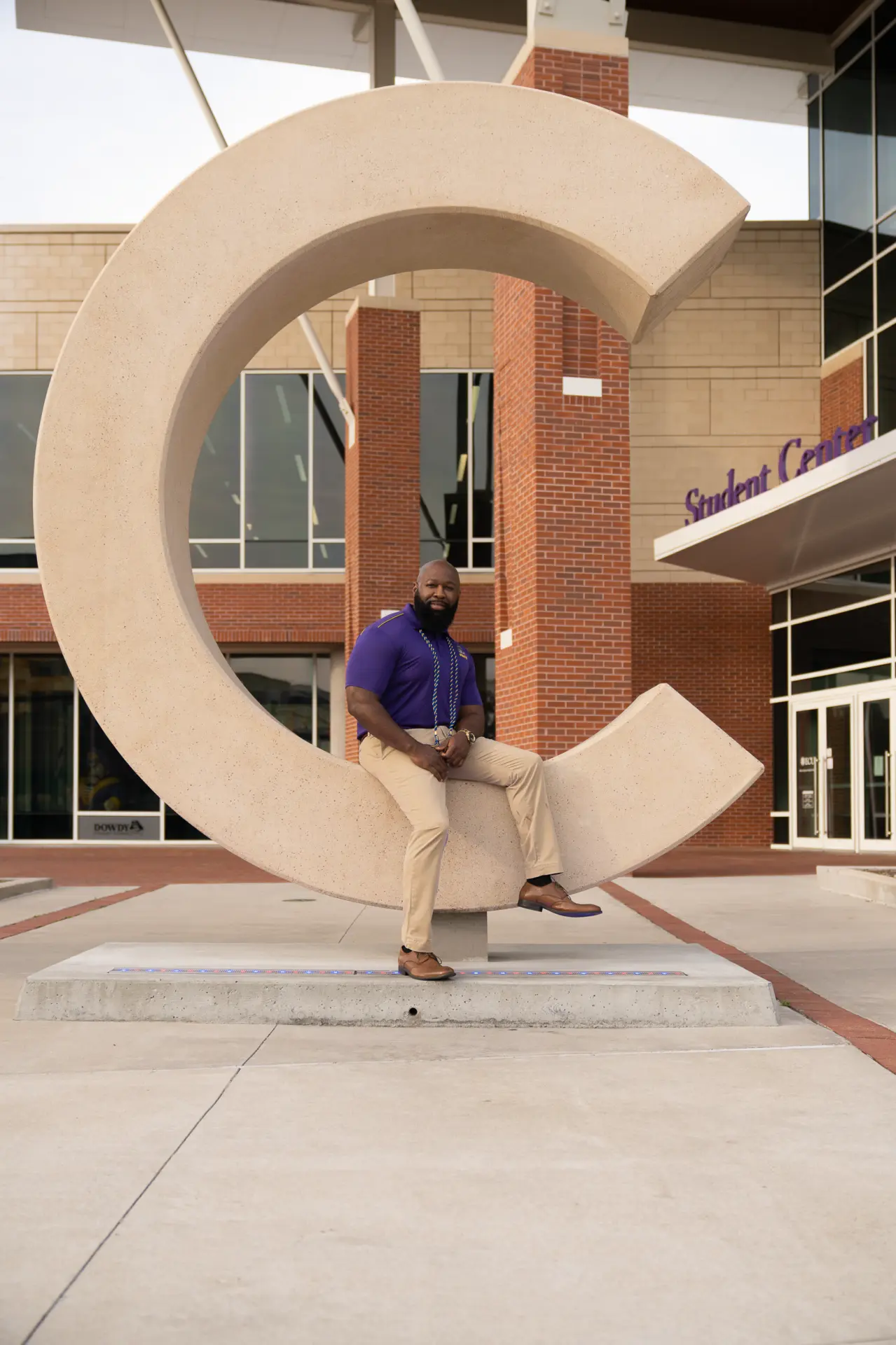 Graduate walking past the ECU C sculpture on campus