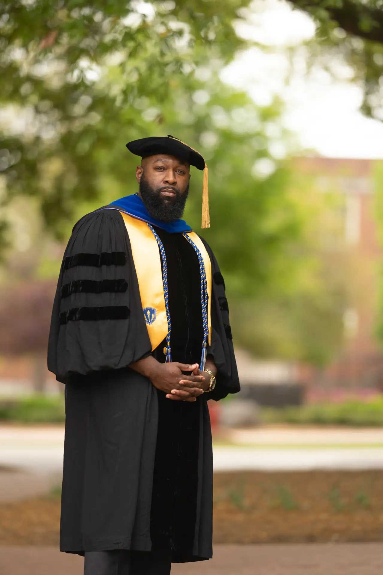 Male graduate in a black gown and stole standing on the grass