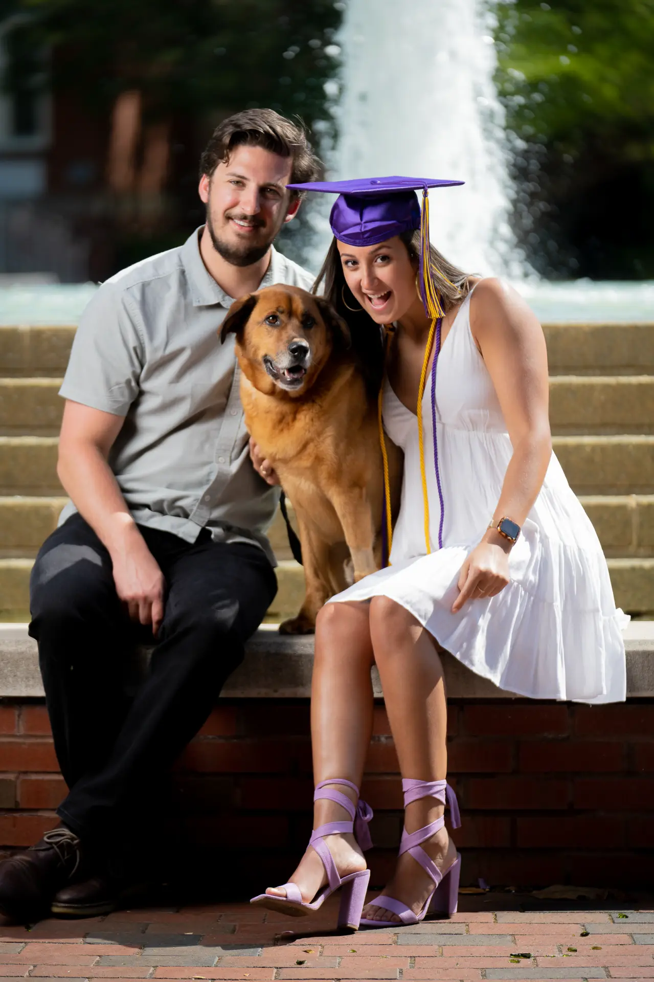 Graduate and family seated on campus steps beside a fountain