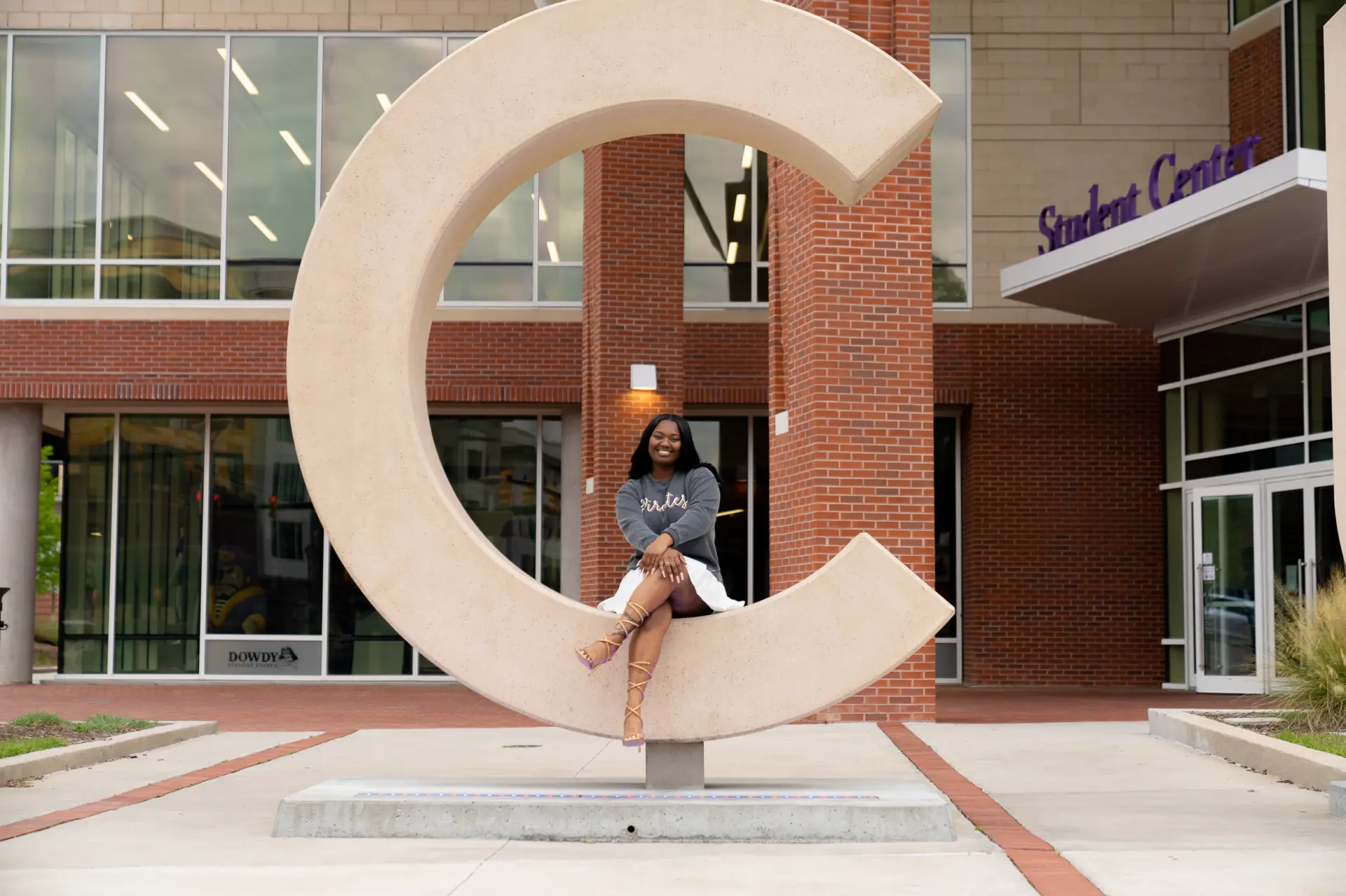 Graduate seated inside the ECU C sculpture outside a campus building