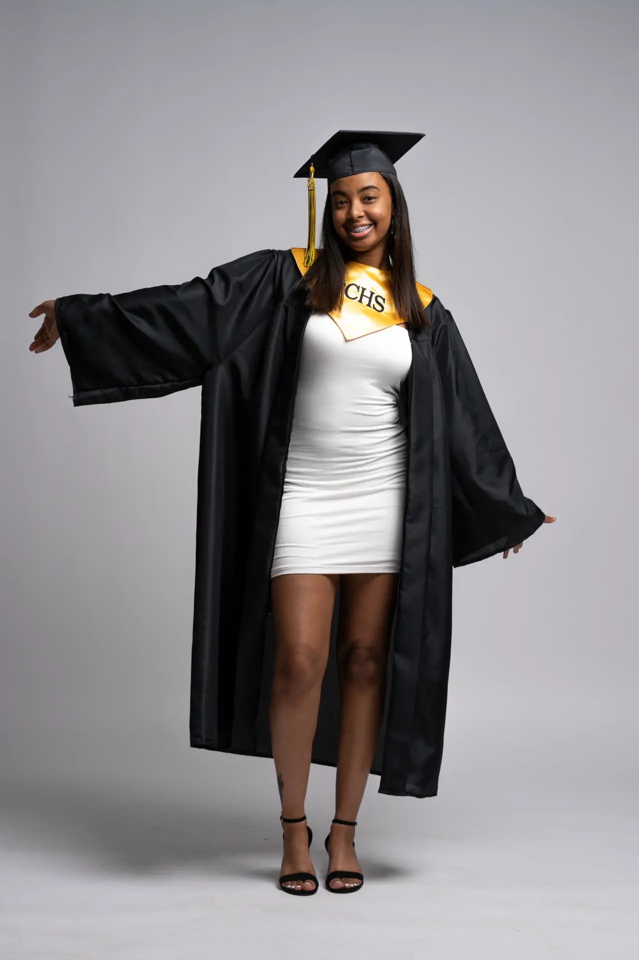 Graduate spreading her black gown open in a playful studio pose