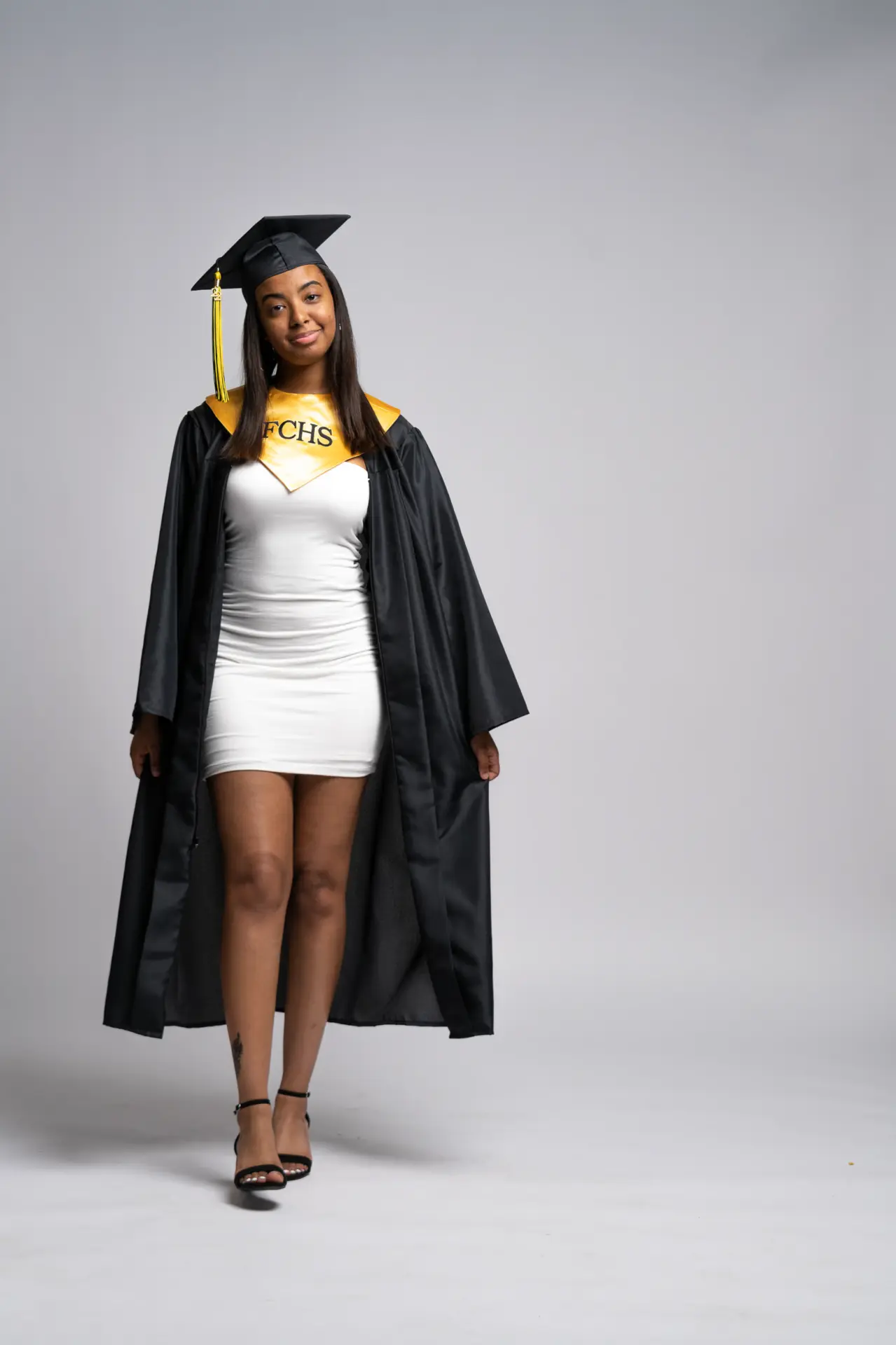 Graduate in a black gown over a white dress, gray studio portrait