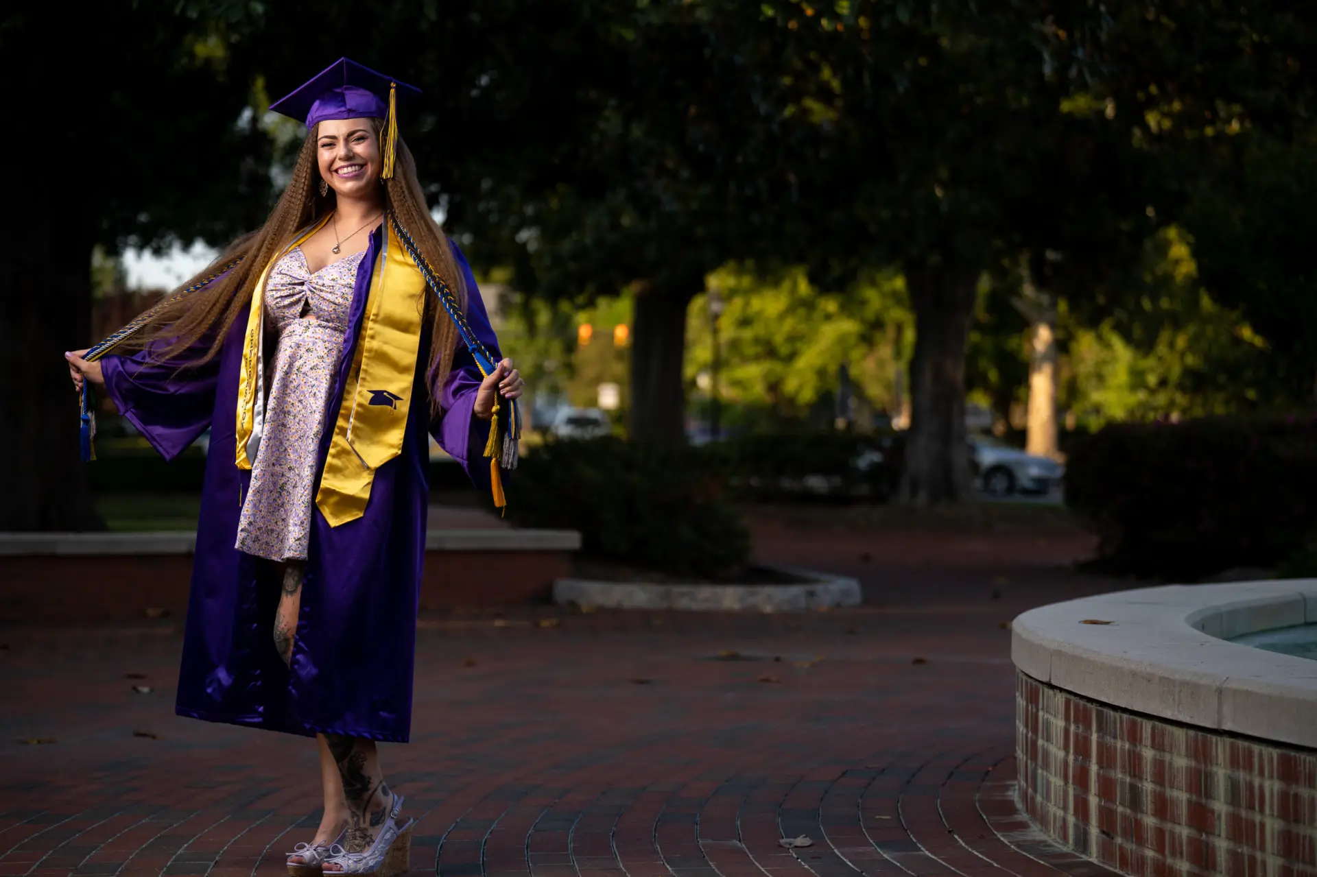 Graduate in a purple gown on a campus plaza at twilight