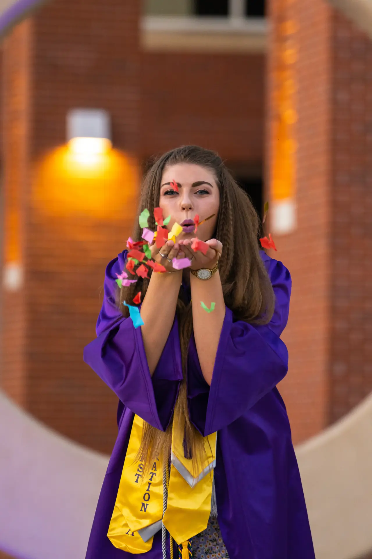 Graduate in purple blowing a kiss beside the ECU C sculpture