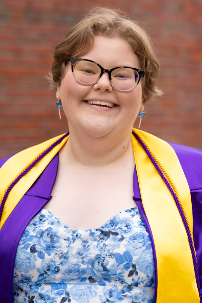 Smiling graduate with glasses in a purple and gold stole