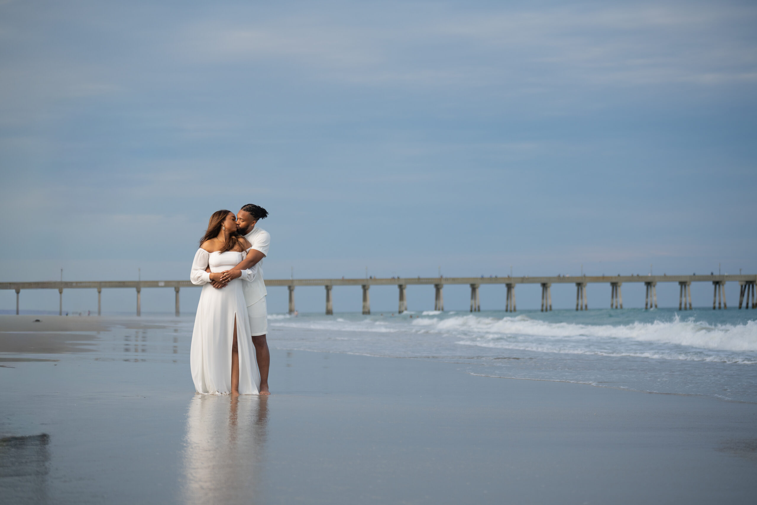 Couple embracing on the beach beside a long pier