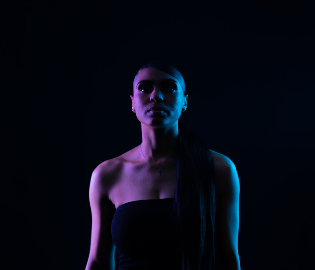 Woman lit with purple and blue gels on a dark backdrop