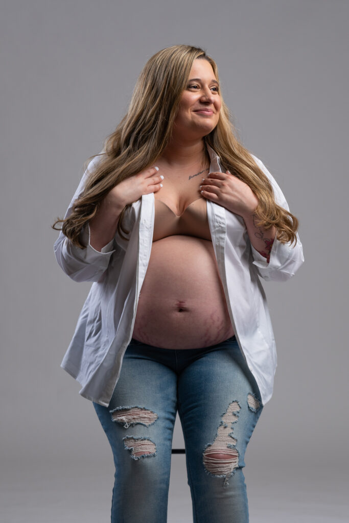 Expectant mother in an open white shirt and jeans, studio portrait
