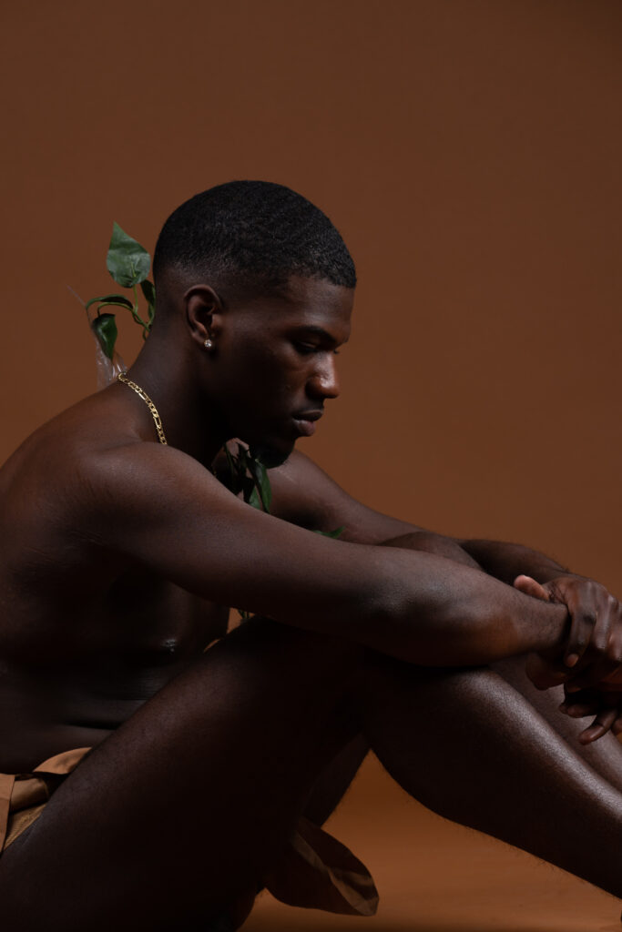 Shirtless man seated on the floor against a warm brown backdrop